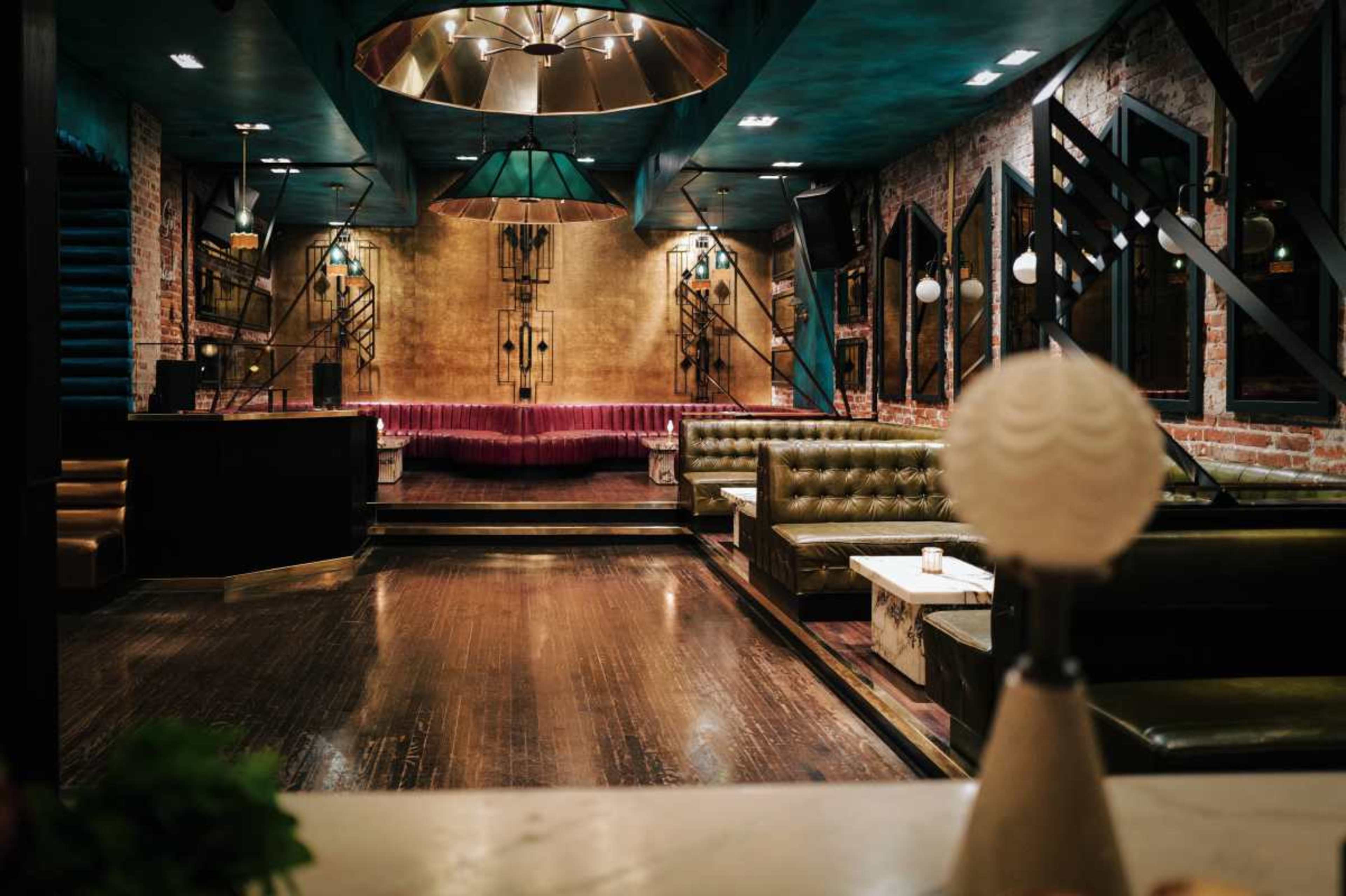 The image shows a dimly lit restaurant interior with exposed brick walls, leather seating, and a decorative bar area.