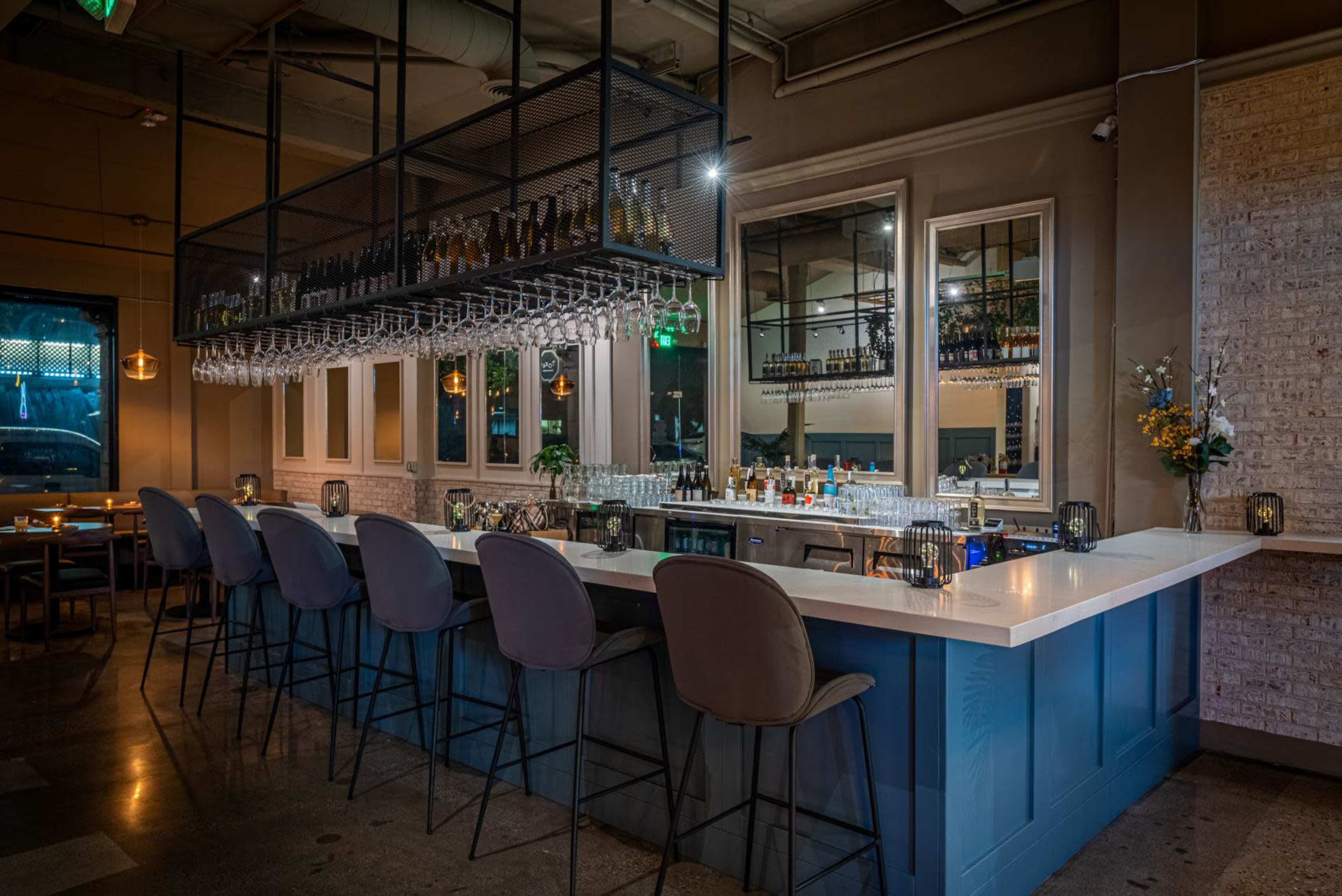 A modern bar area with a white countertop, bar stools, and a rack of wine bottles overhead.