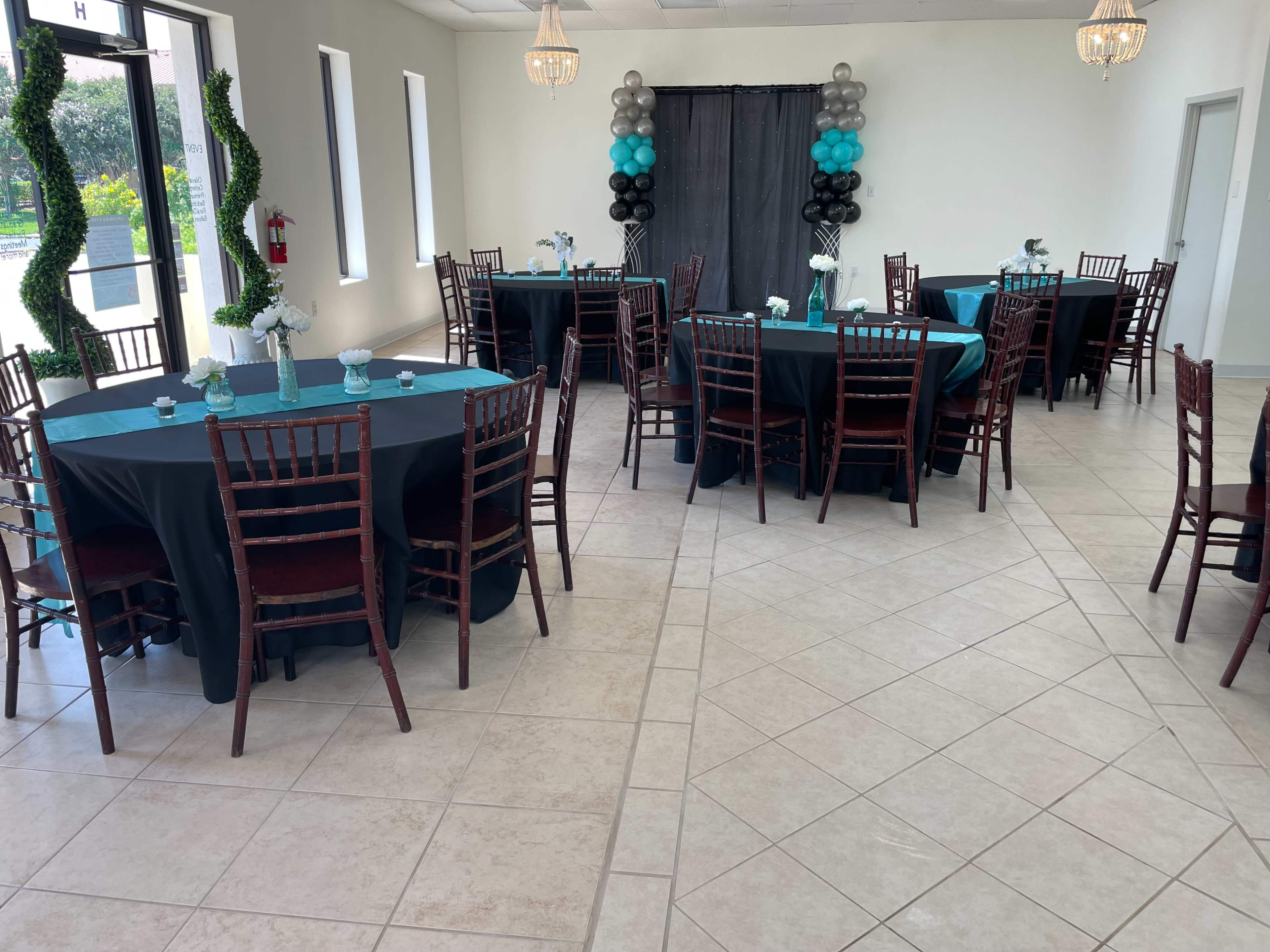 A banquet hall set up with several round tables covered in black tablecloths with teal accents, arranged neatly around the room.