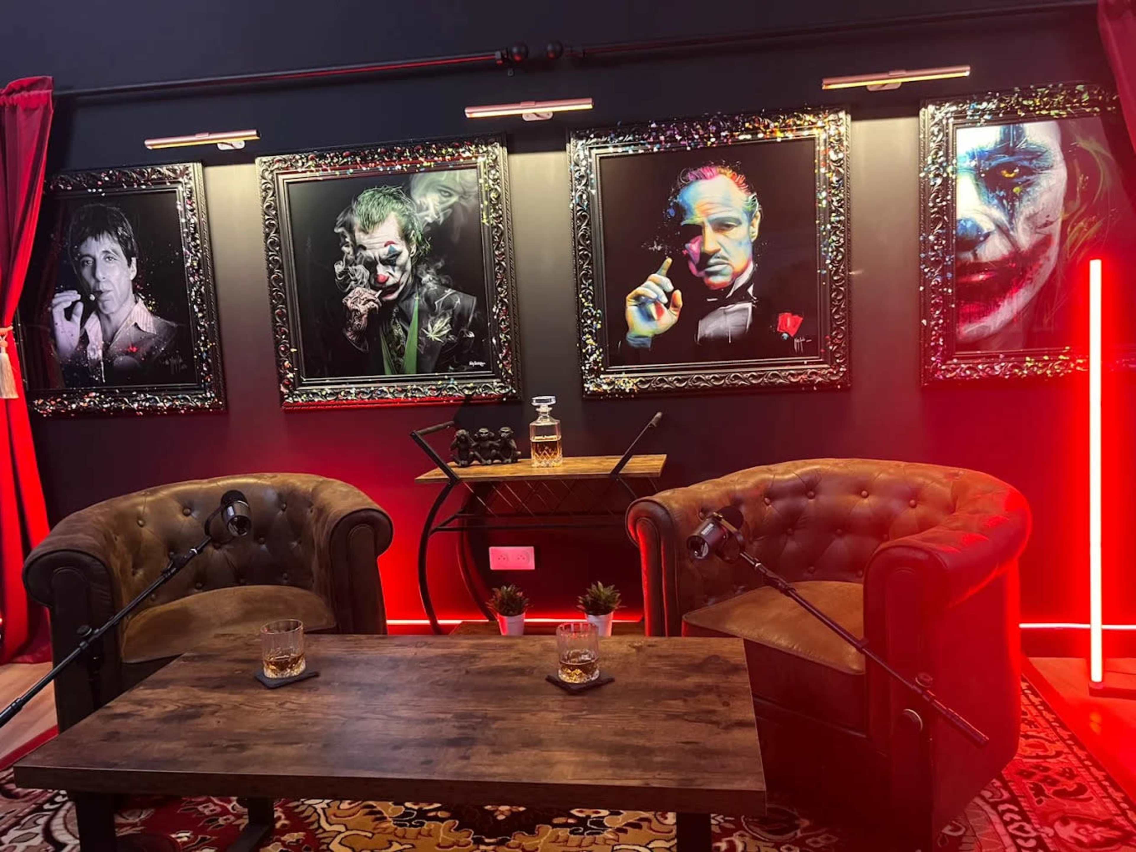 The image shows a dimly lit room featuring two leather armchairs facing a wooden coffee table, with four framed portraits of iconic film characters on the wall behind.