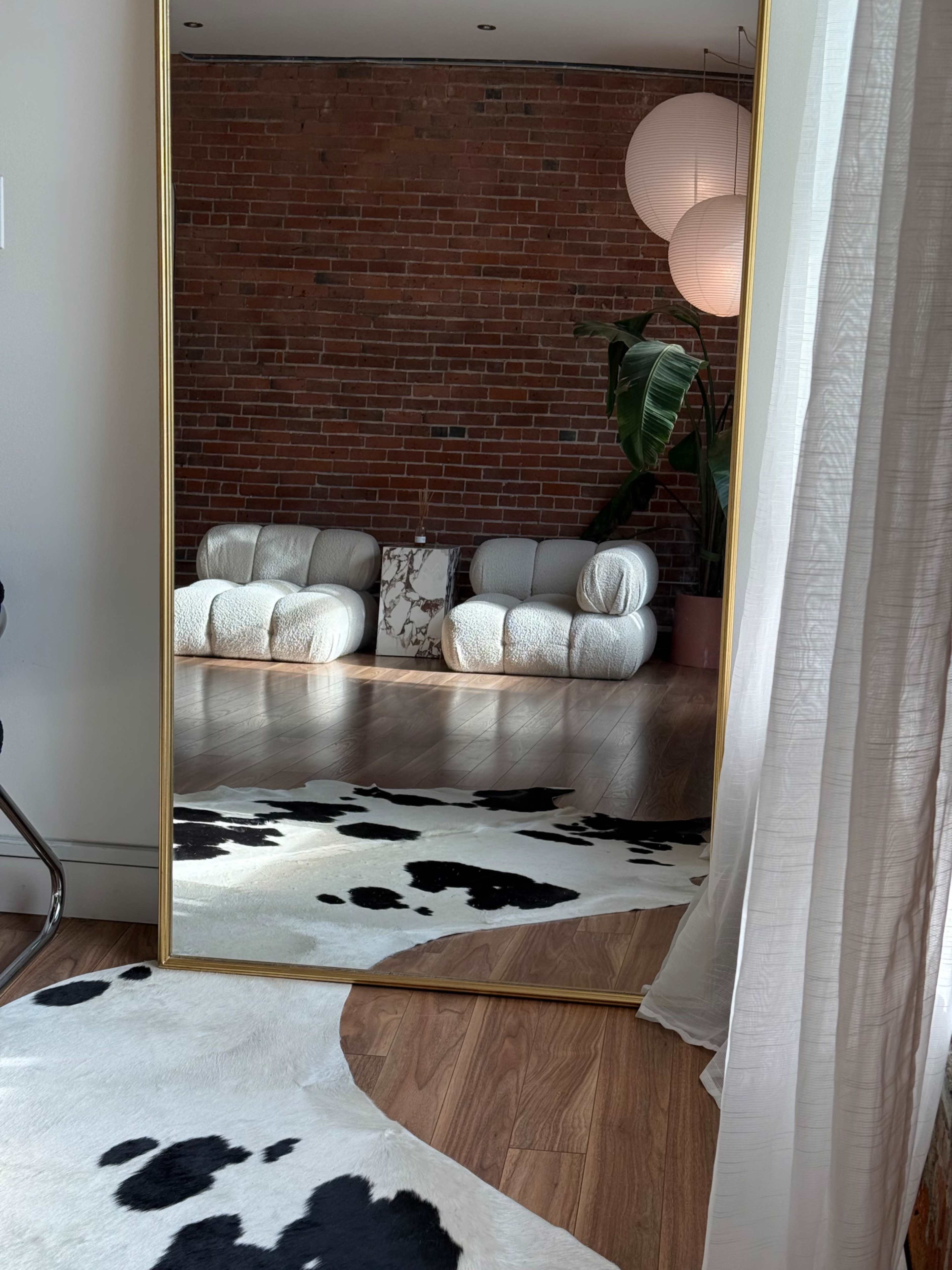 A large mirror reflects a brick wall, two modern sofas, and a patterned rug on the wooden floor.