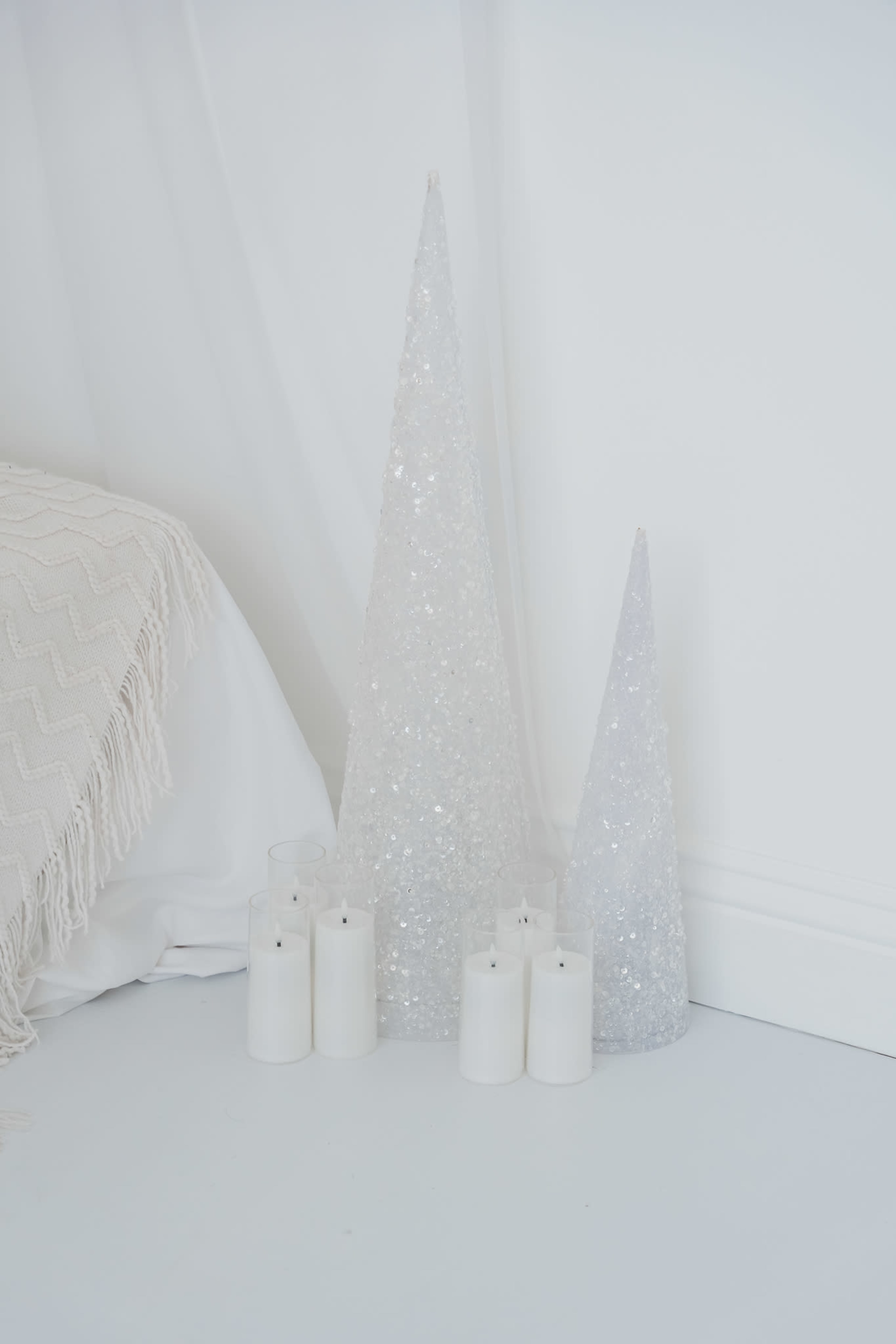 The image shows two sparkling Christmas tree shapes alongside several white candles on a plain white background.