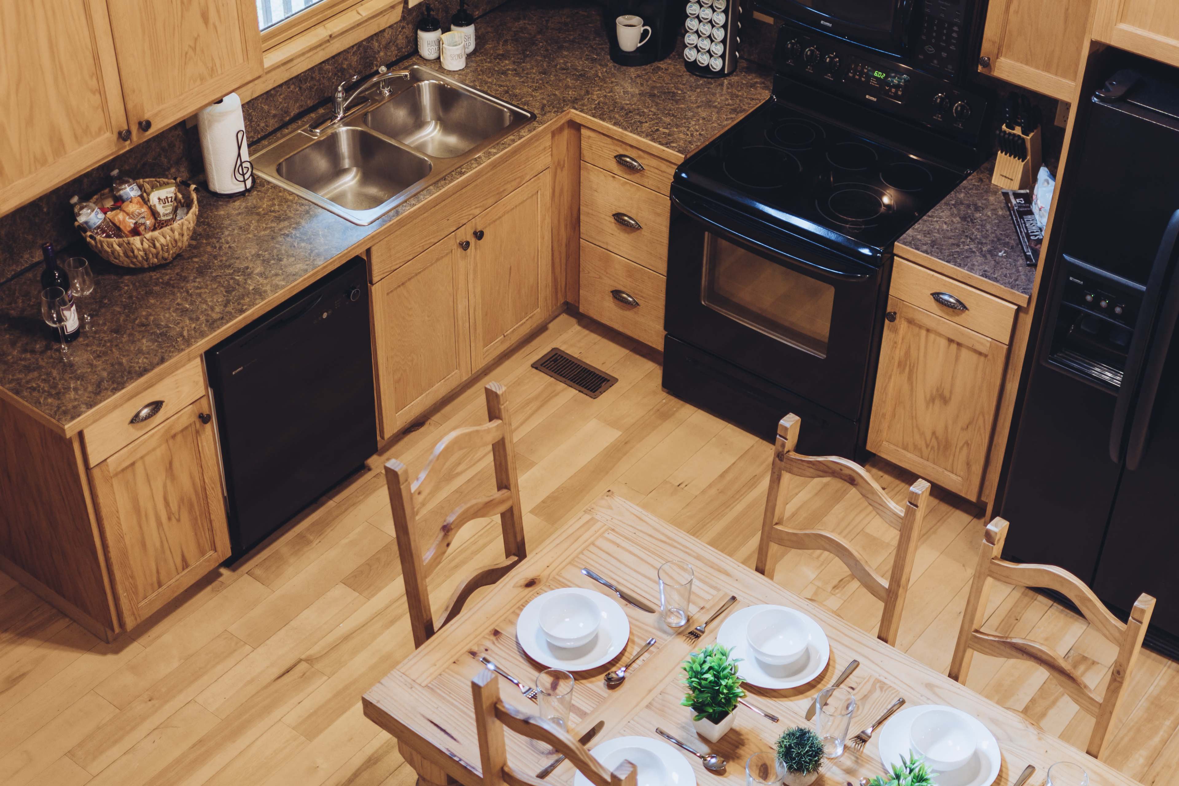 A well-organized kitchen features wooden cabinets, a black stove and dishwasher, a double sink, and a dining table set for a meal.