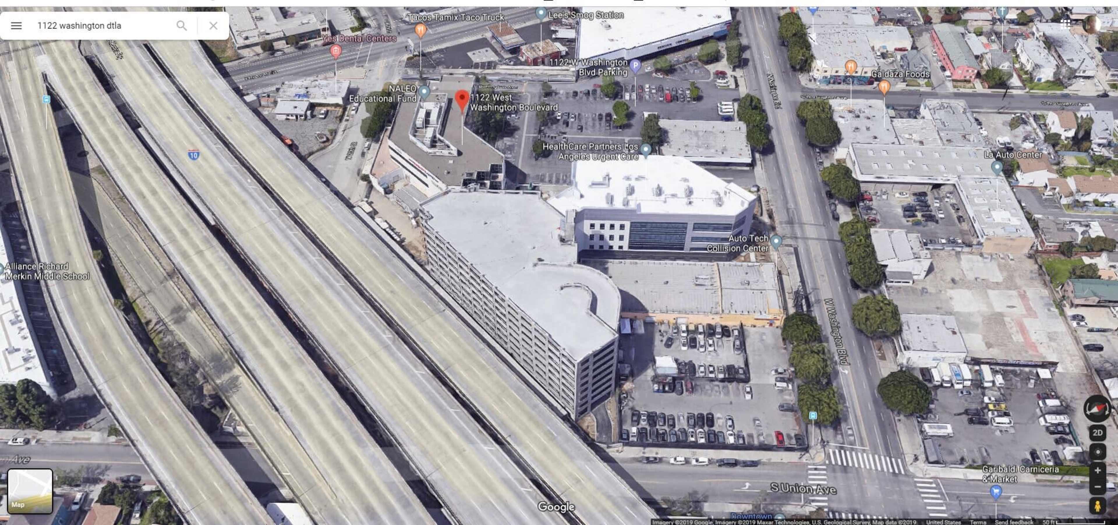 The image shows an aerial view of a highway interchange adjacent to a commercial area with several buildings and a parking lot.