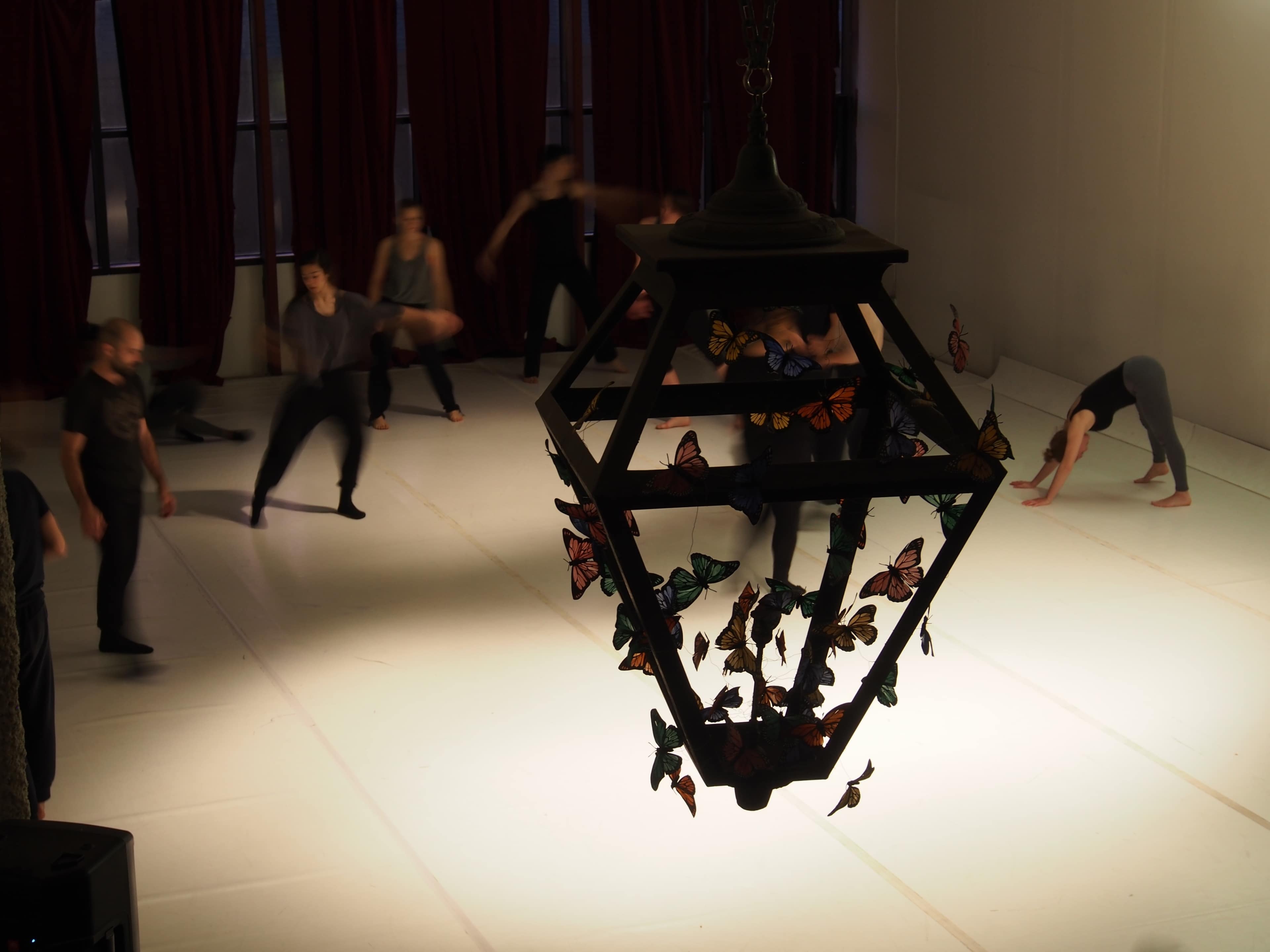A modern dance class takes place in a studio with a large chandelier adorned with butterfly decorations.