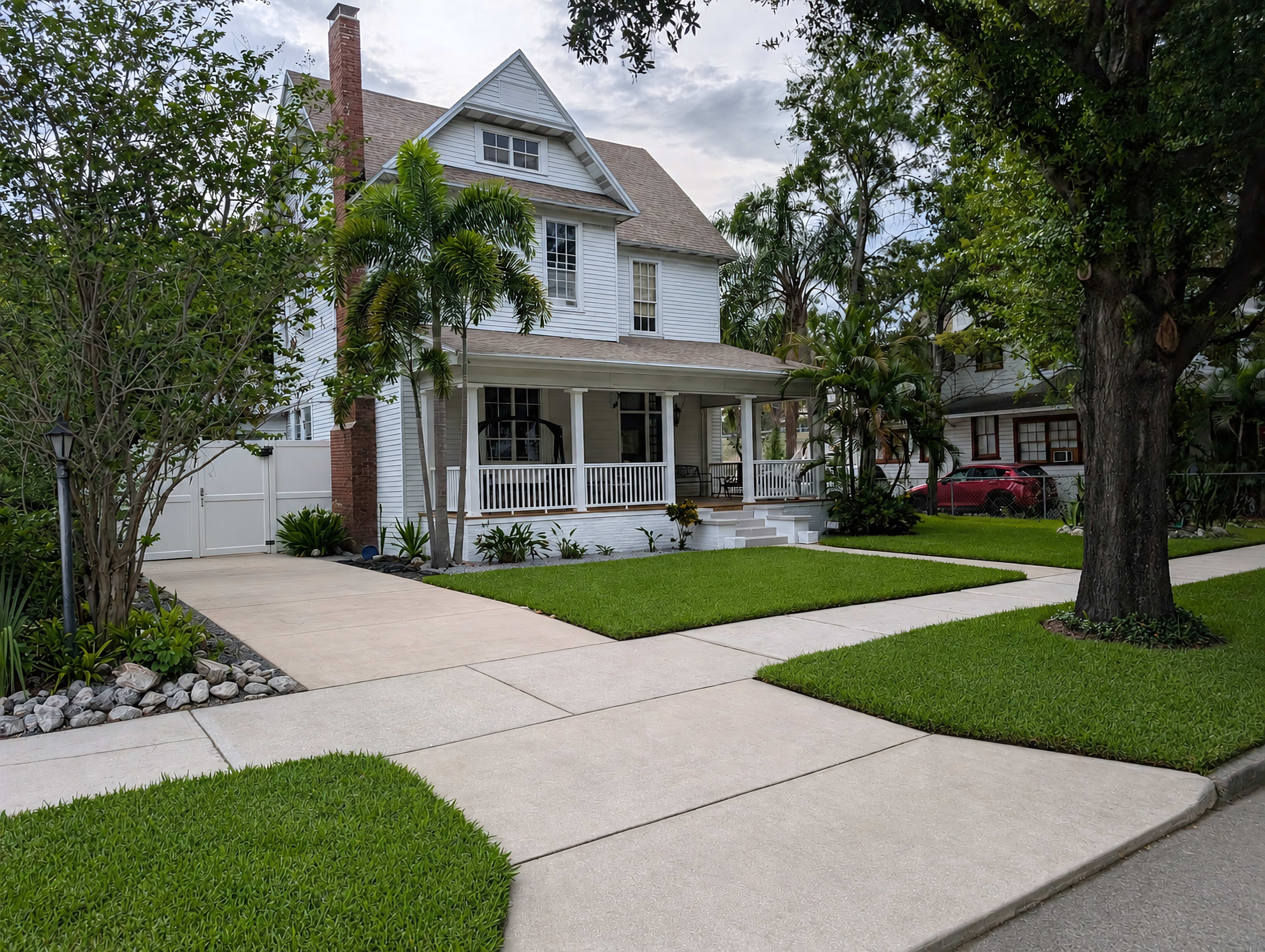 The image features a large, two-story white house with a porch, set among well-maintained lawns and decorative landscaping.
