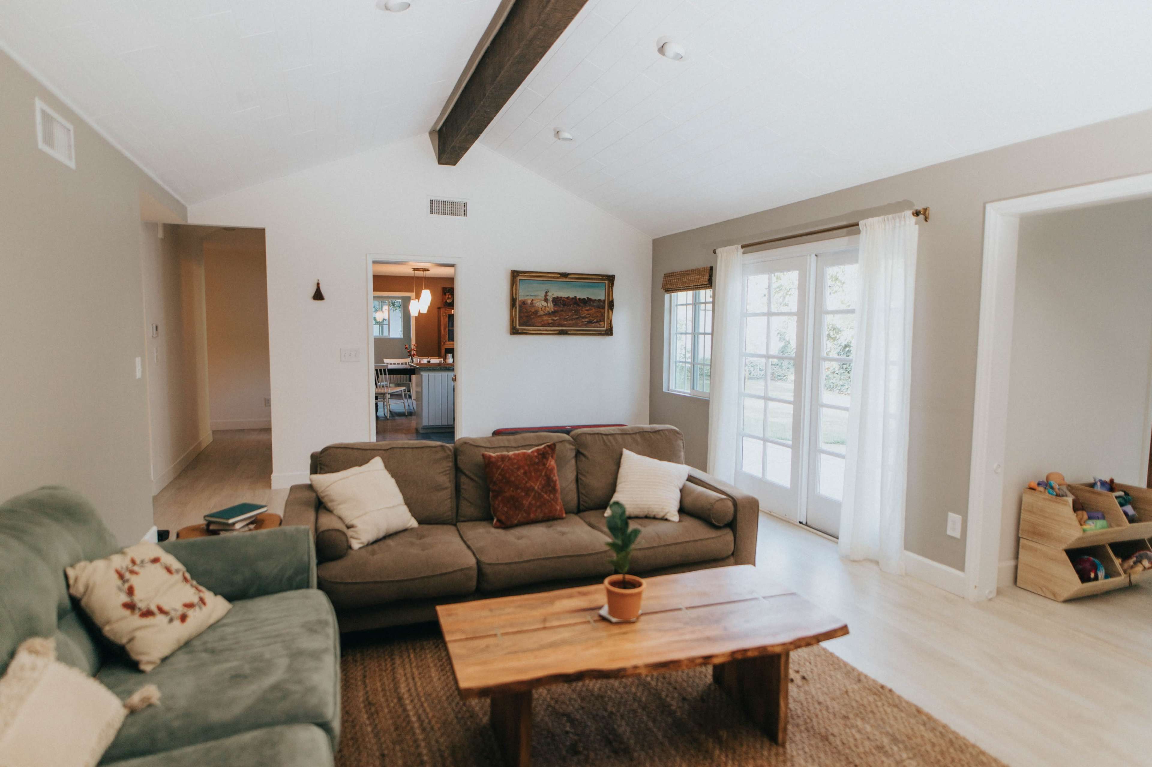 The image shows a living room with a beige couch, a wooden coffee table, and large windows leading to a patio area.