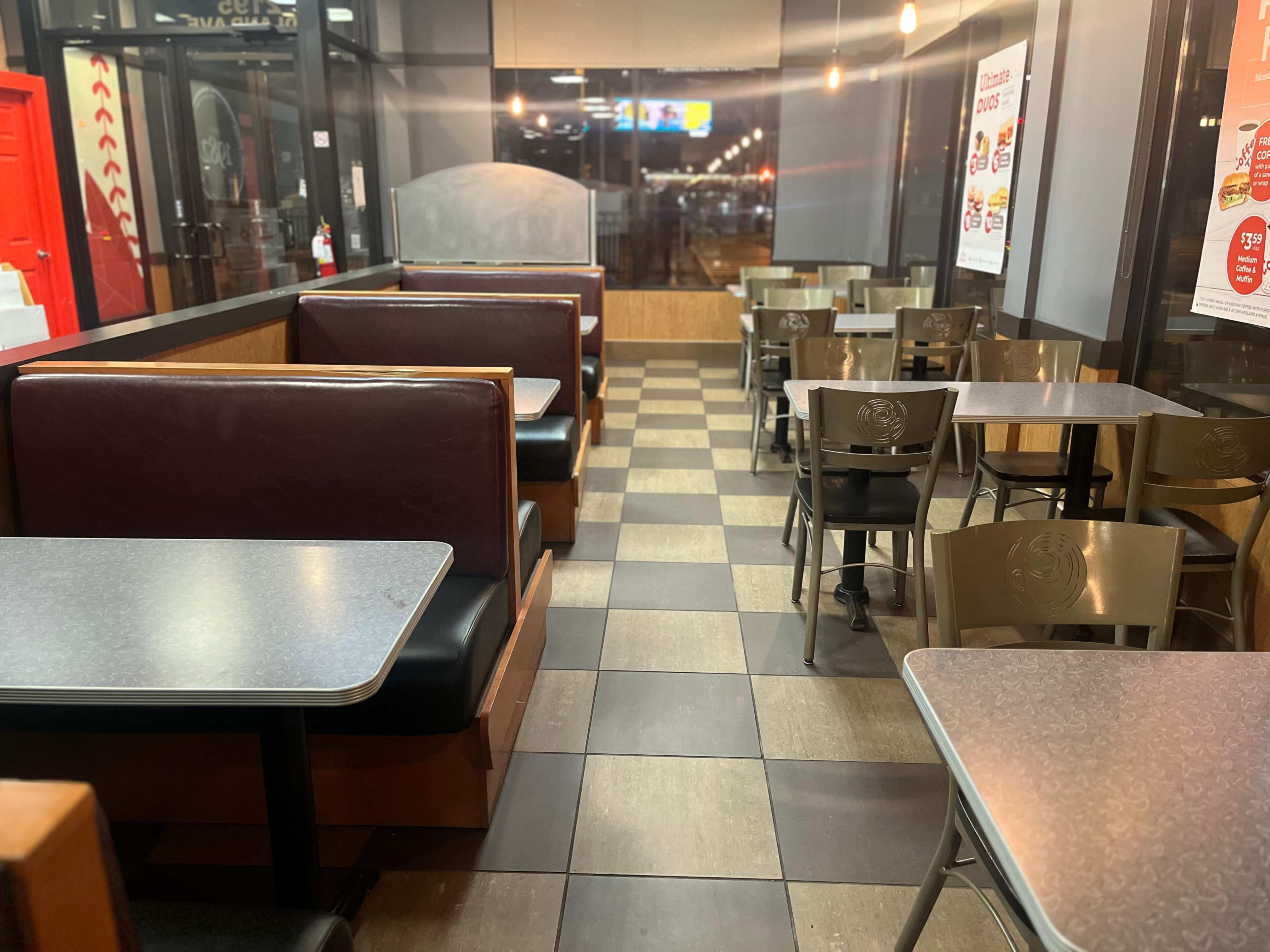 The image shows an empty fast-food restaurant with booth seating and metal tables arranged on a tiled floor.