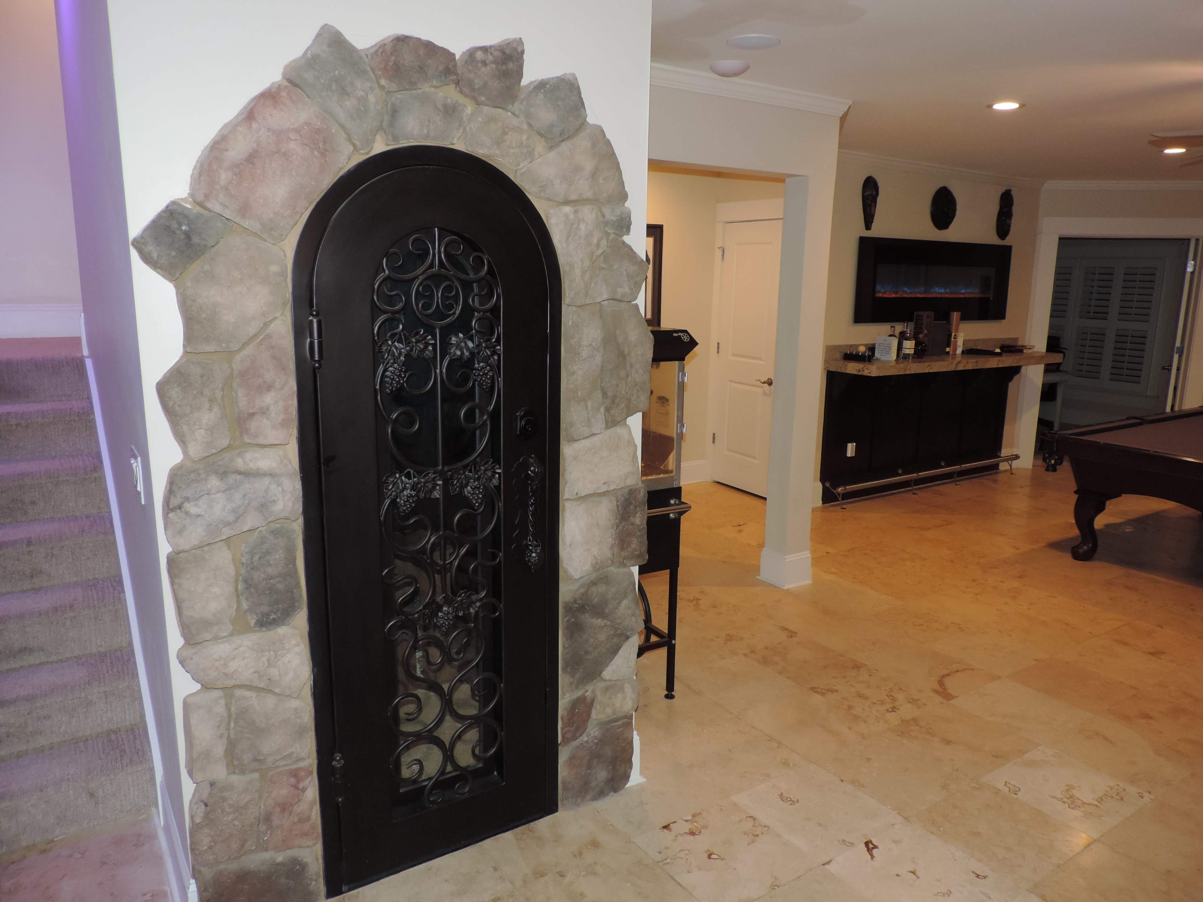 The image shows a decorative arched door made of wrought iron set within a stone archway, leading into a well-lit interior space with a bar and pool table.