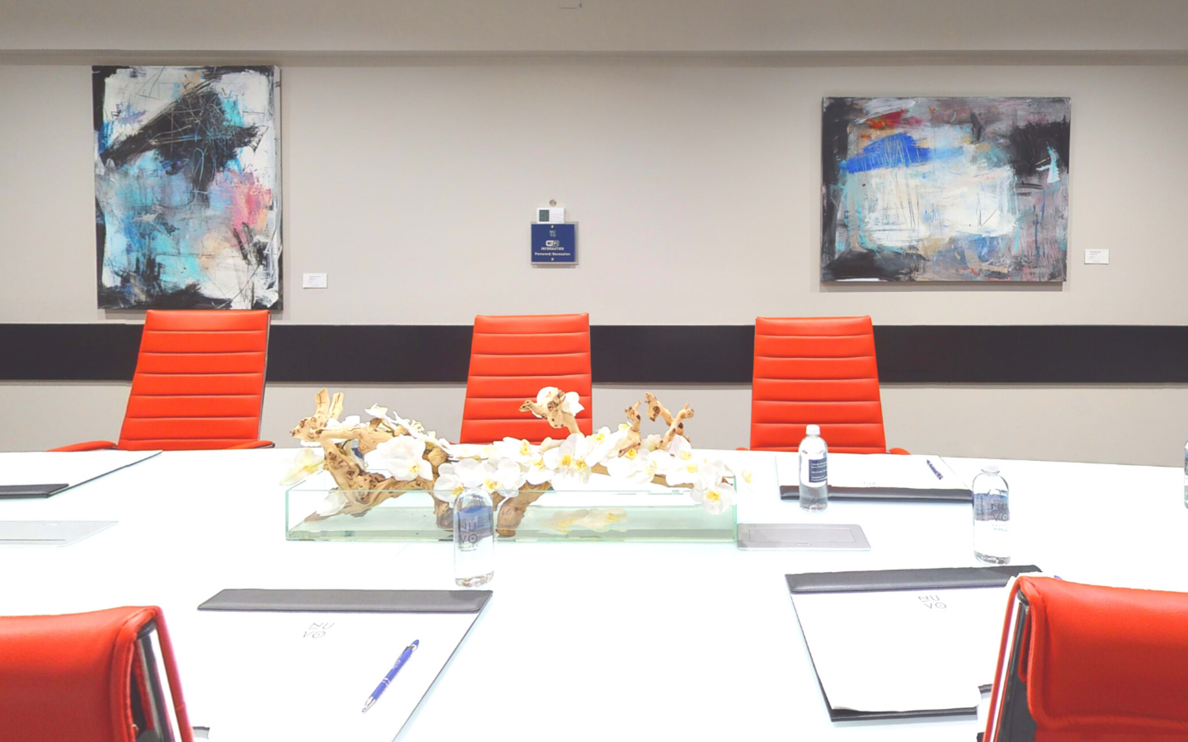 A modern conference room with a white table, red chairs, and two abstract paintings on the walls.