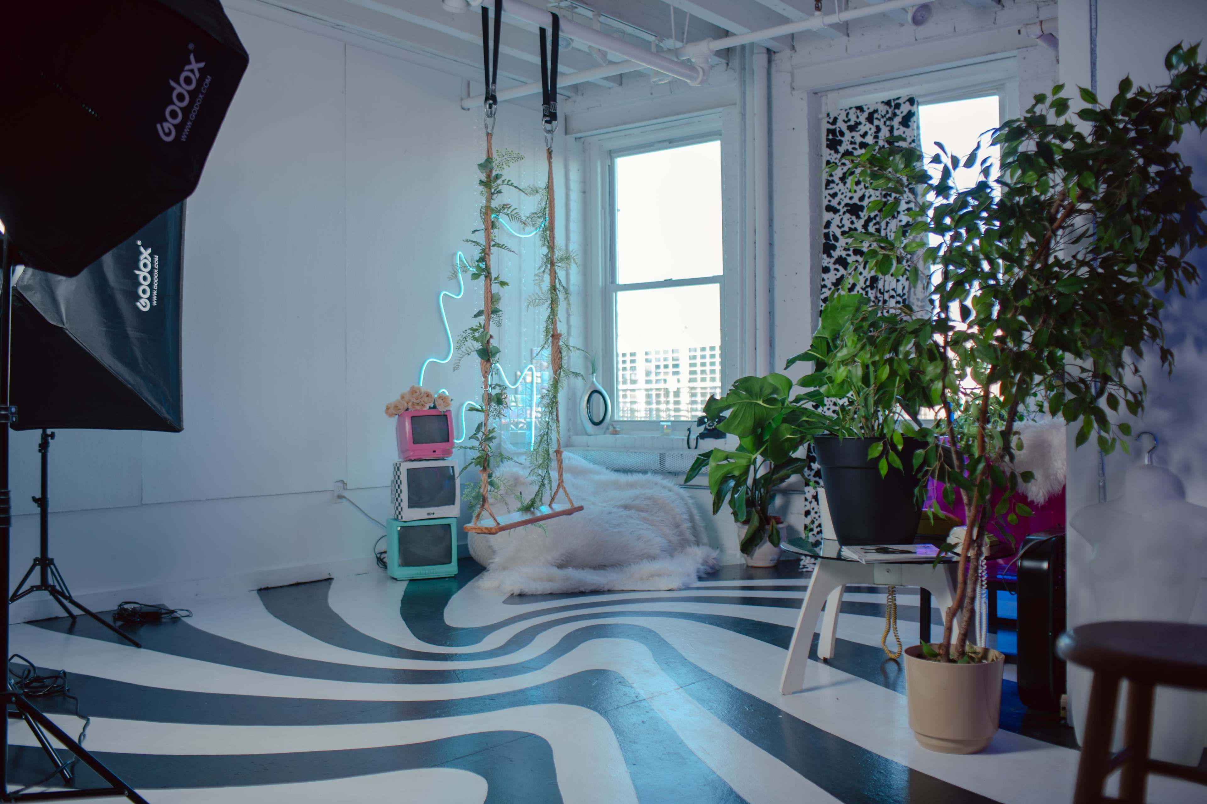 A modern, minimalist interior space with a patterned floor, large windows, a swing, neon lights, and various plants.