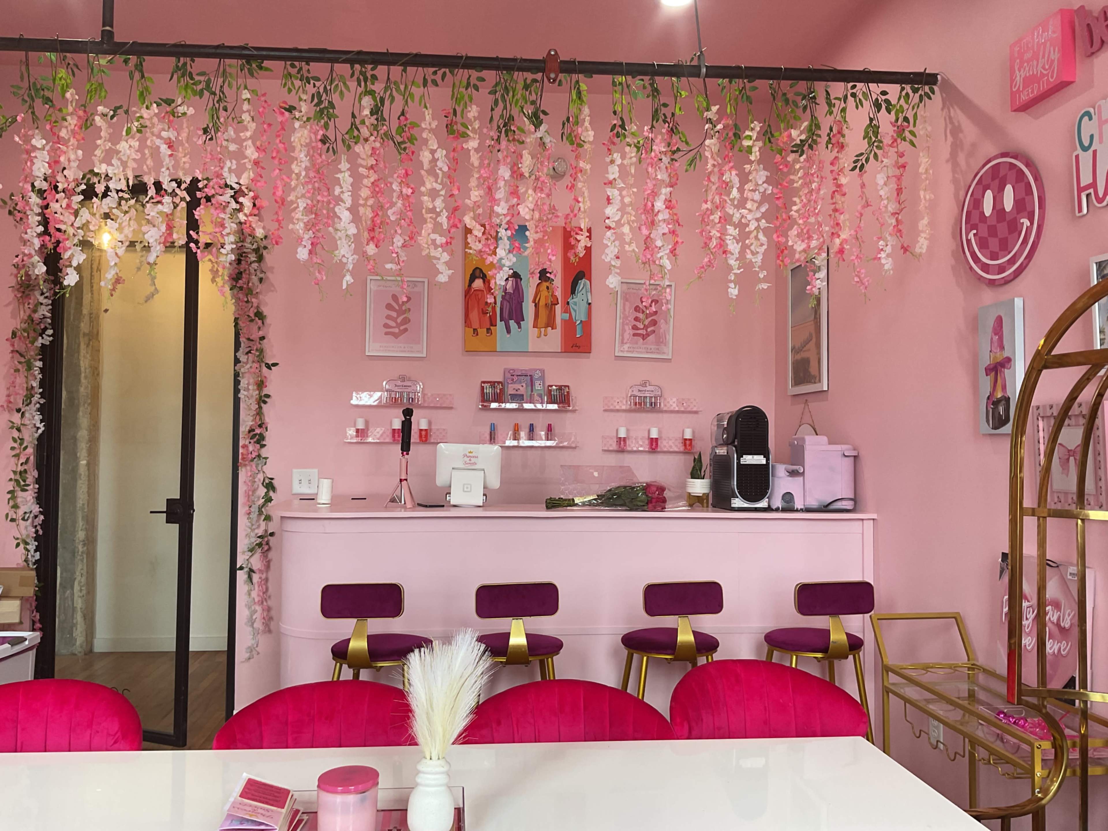 The interior features a pink-themed space with floral decorations hanging from the ceiling, a bar area with beauty products, and pink seating.