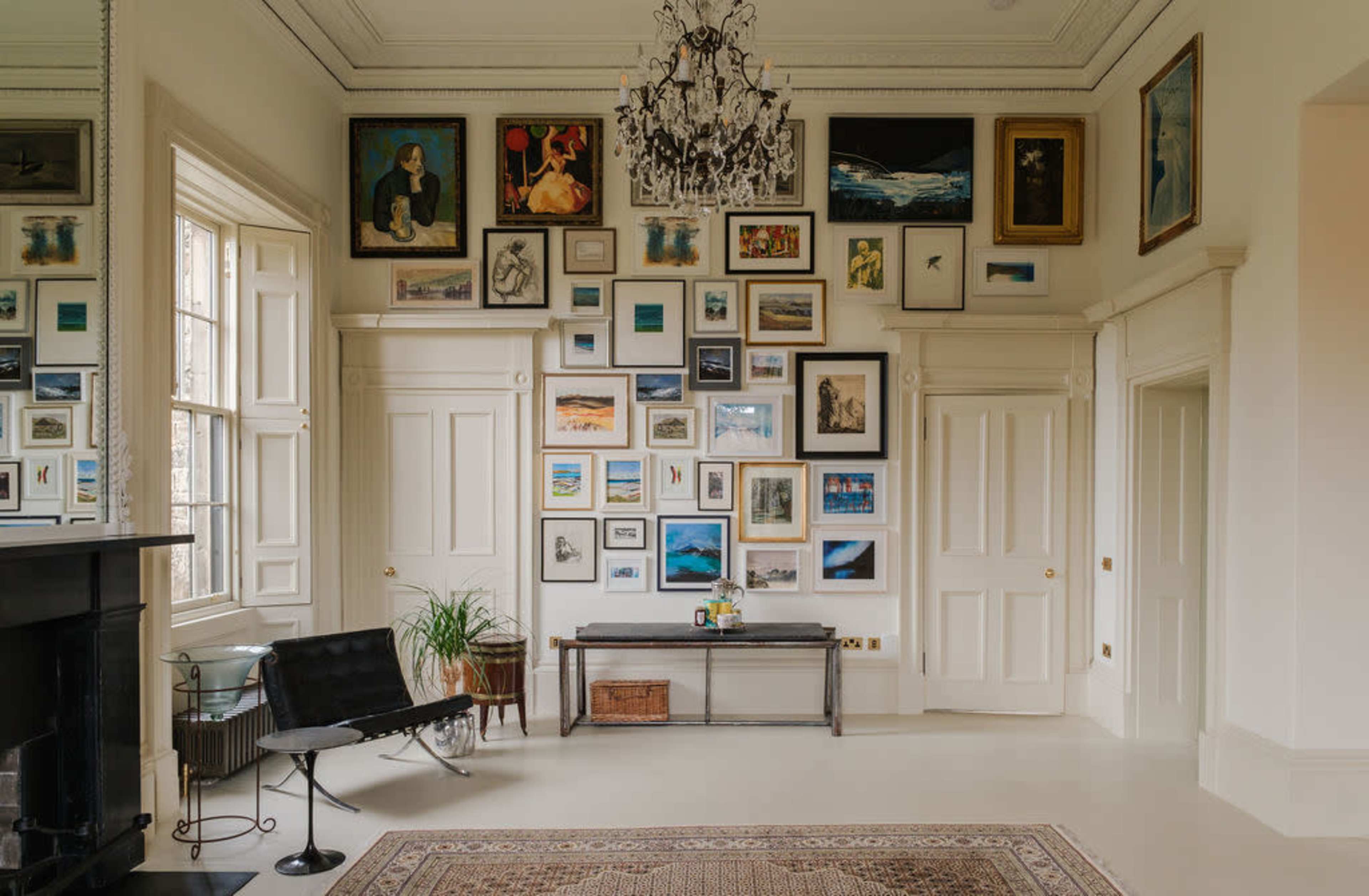 The image shows a brightly lit room featuring a wall adorned with various framed artworks, a sleek chair, a small table, and a decorative rug on the floor.