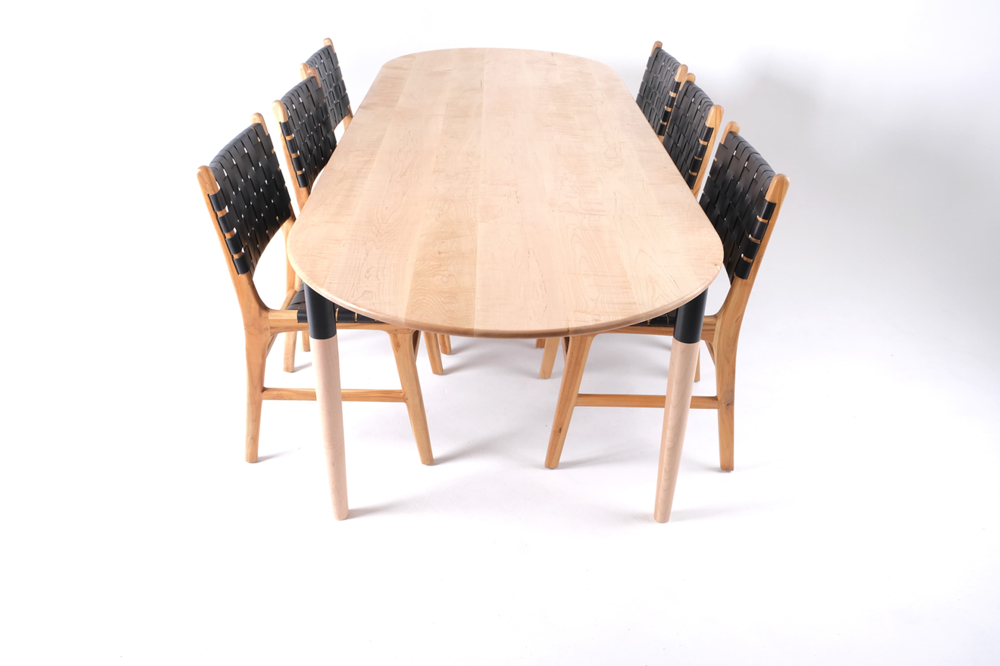 A wooden oval dining table is surrounded by six black and wooden chairs.