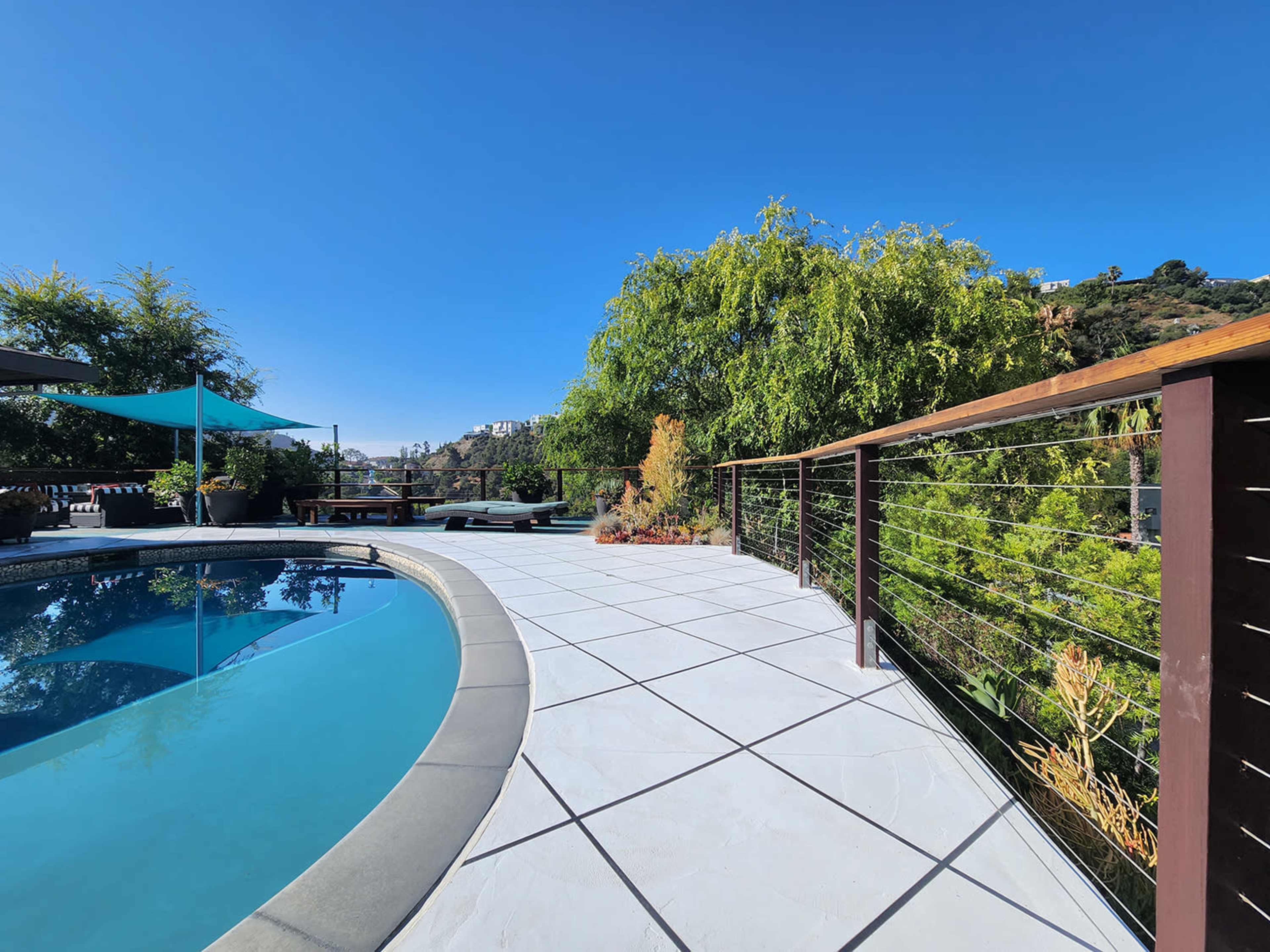 A swimming pool surrounded by a patio, with greenery in the background and a blue sky above.