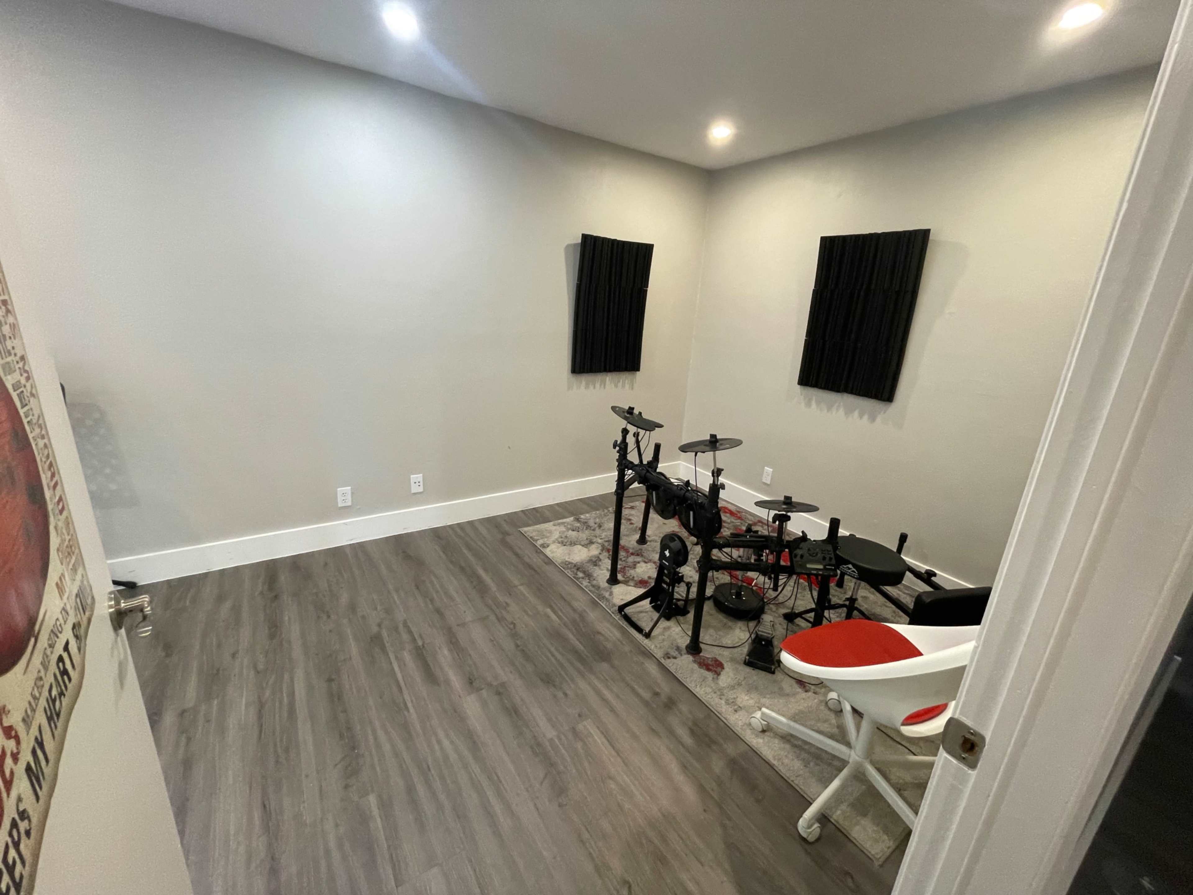 A small, empty practice room featuring an electronic drum kit, a chair, and soundproofing panels on the walls.