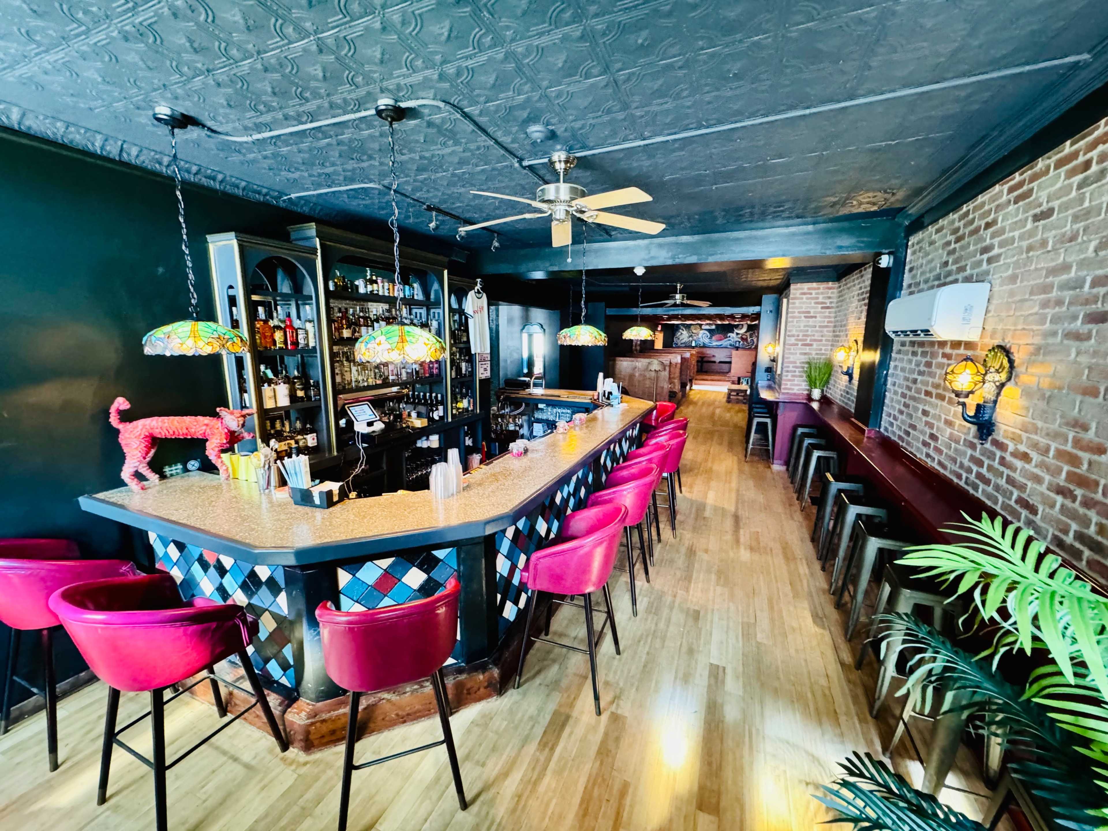 A bar interior with a colorful tiled counter, decorative lighting, and a variety of seating options along the walls.