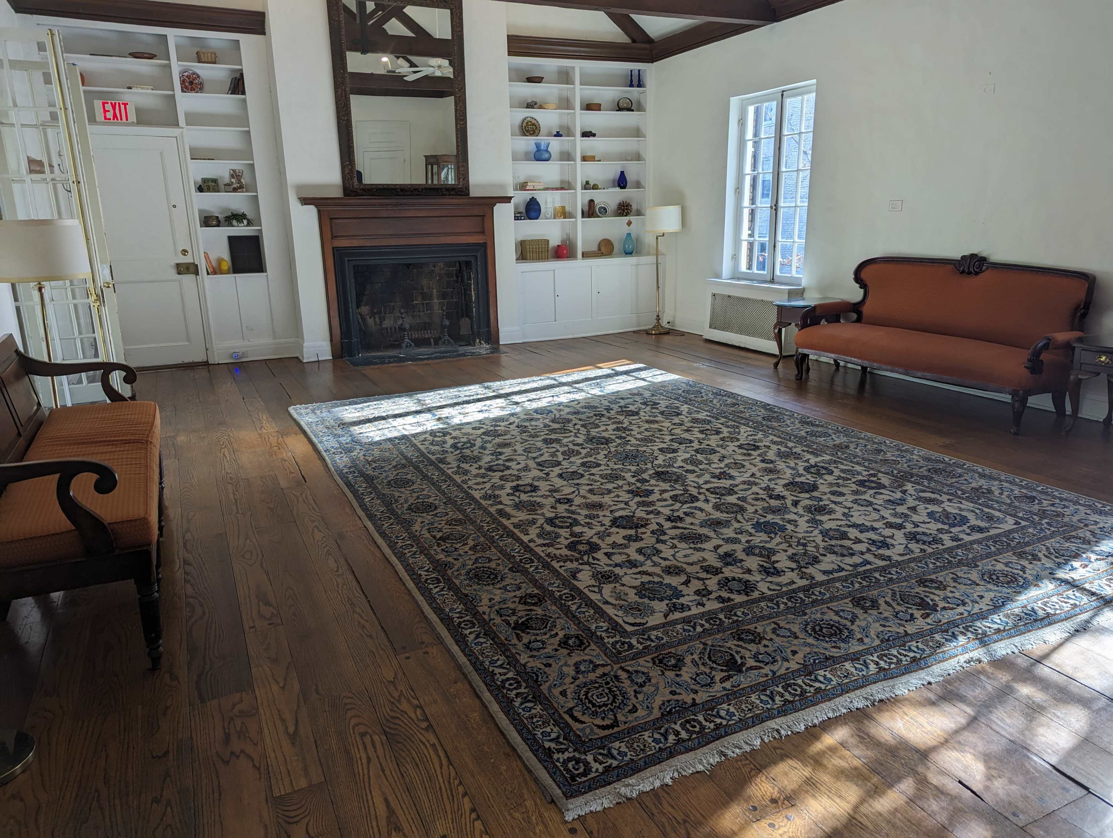 A spacious room with wooden flooring, a large patterned rug, a fireplace surrounded by a mirror, and two upholstered sofas.