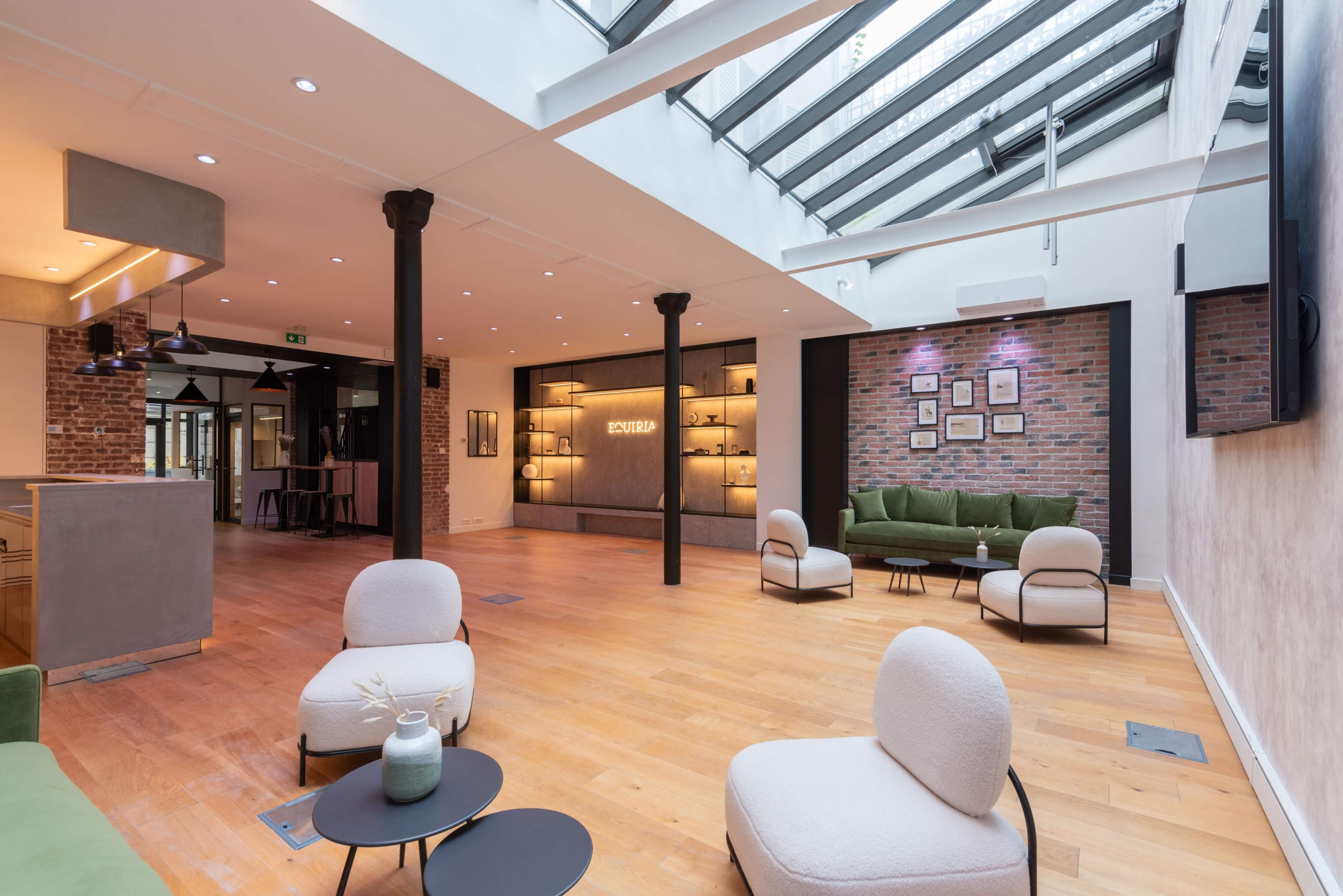 The image shows a modern interior space with wooden flooring, featuring green sofas, minimalist chairs, and a glass ceiling that allows natural light to flood in.