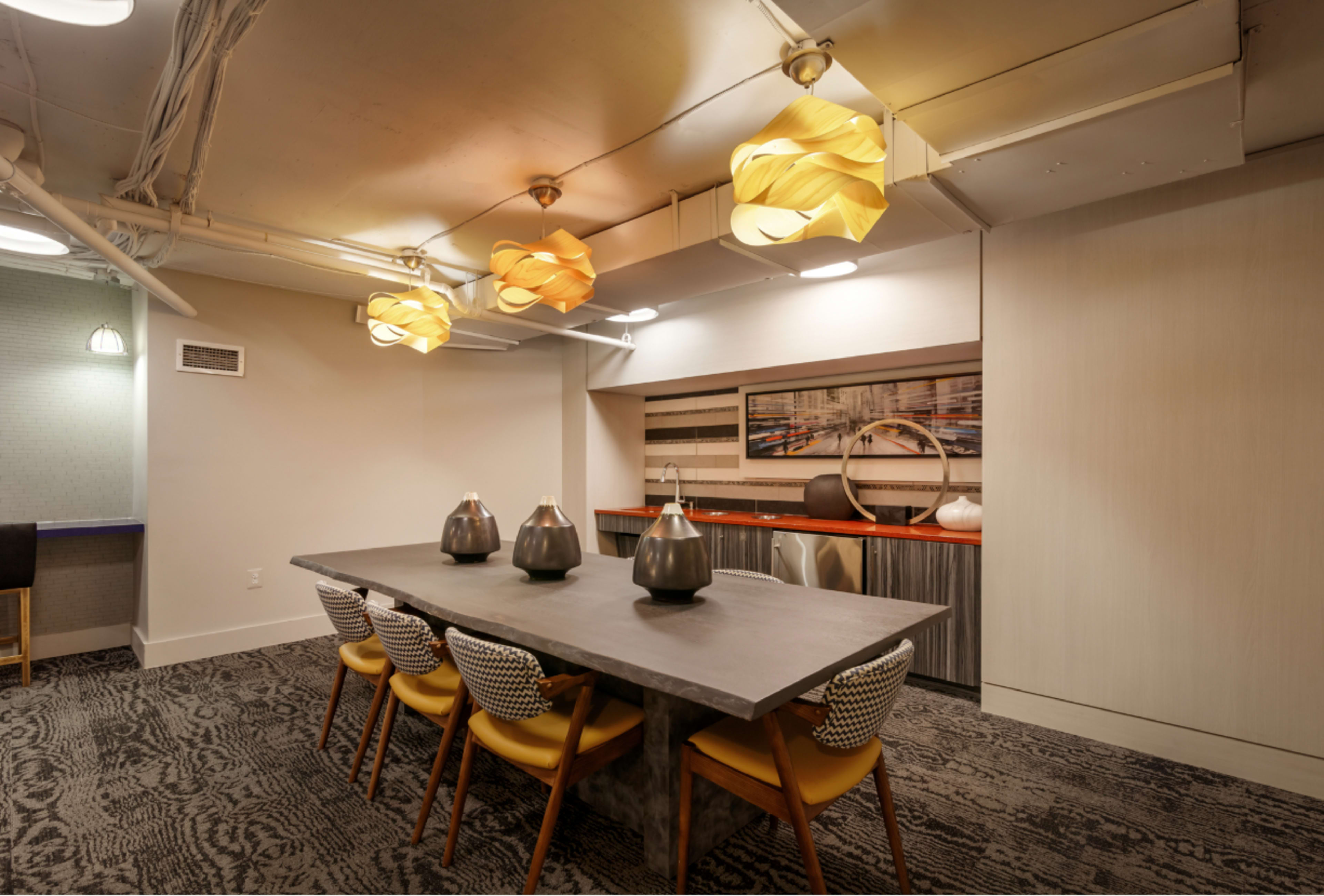 The image shows a modern dining area with a long rectangular table, decorative vases, and unique light fixtures hanging from the ceiling.