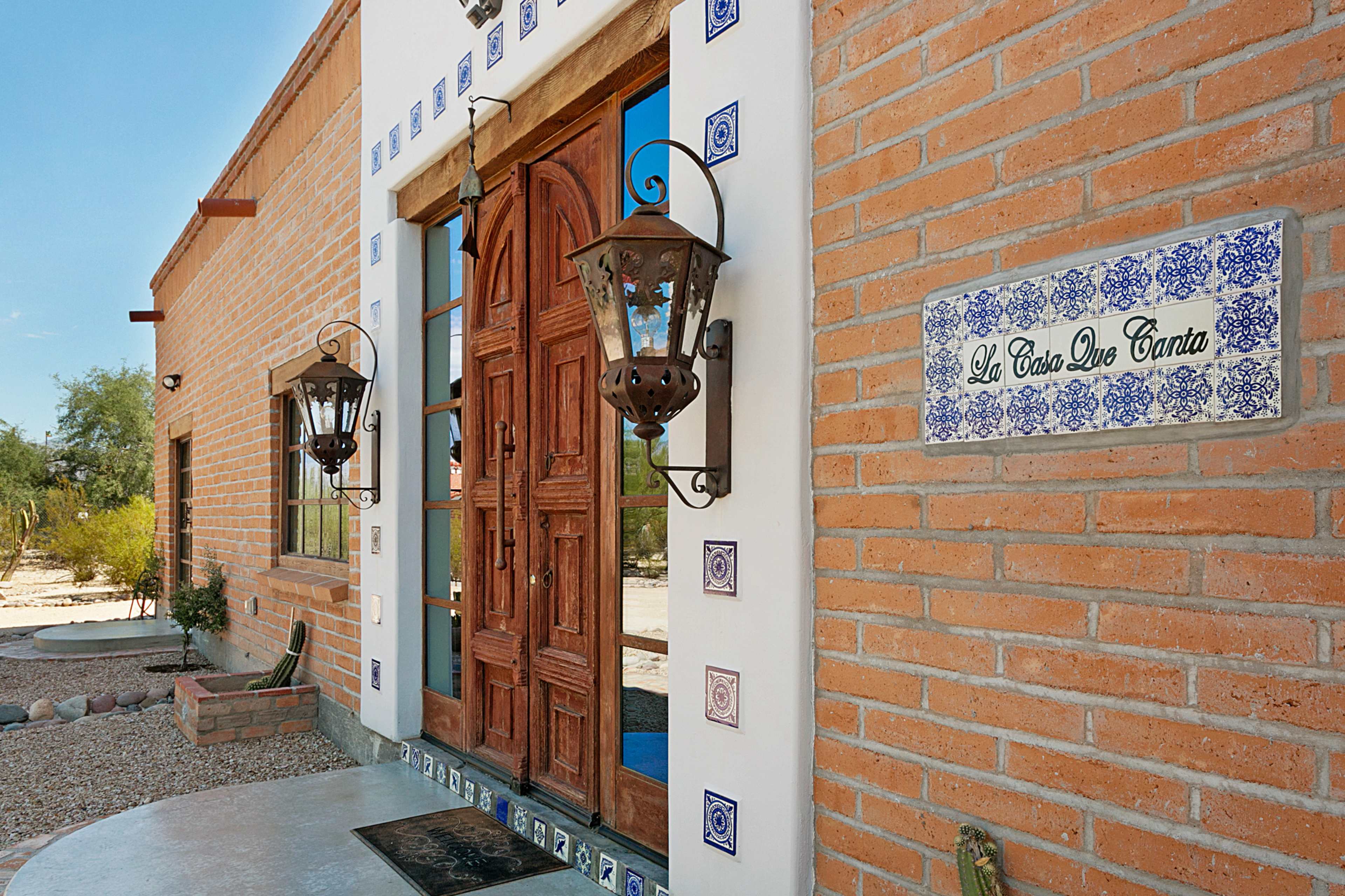 A brick exterior of a house featuring wooden double doors with decorative lanterns and a tiled nameplate reading "La Casa De Tijuana."