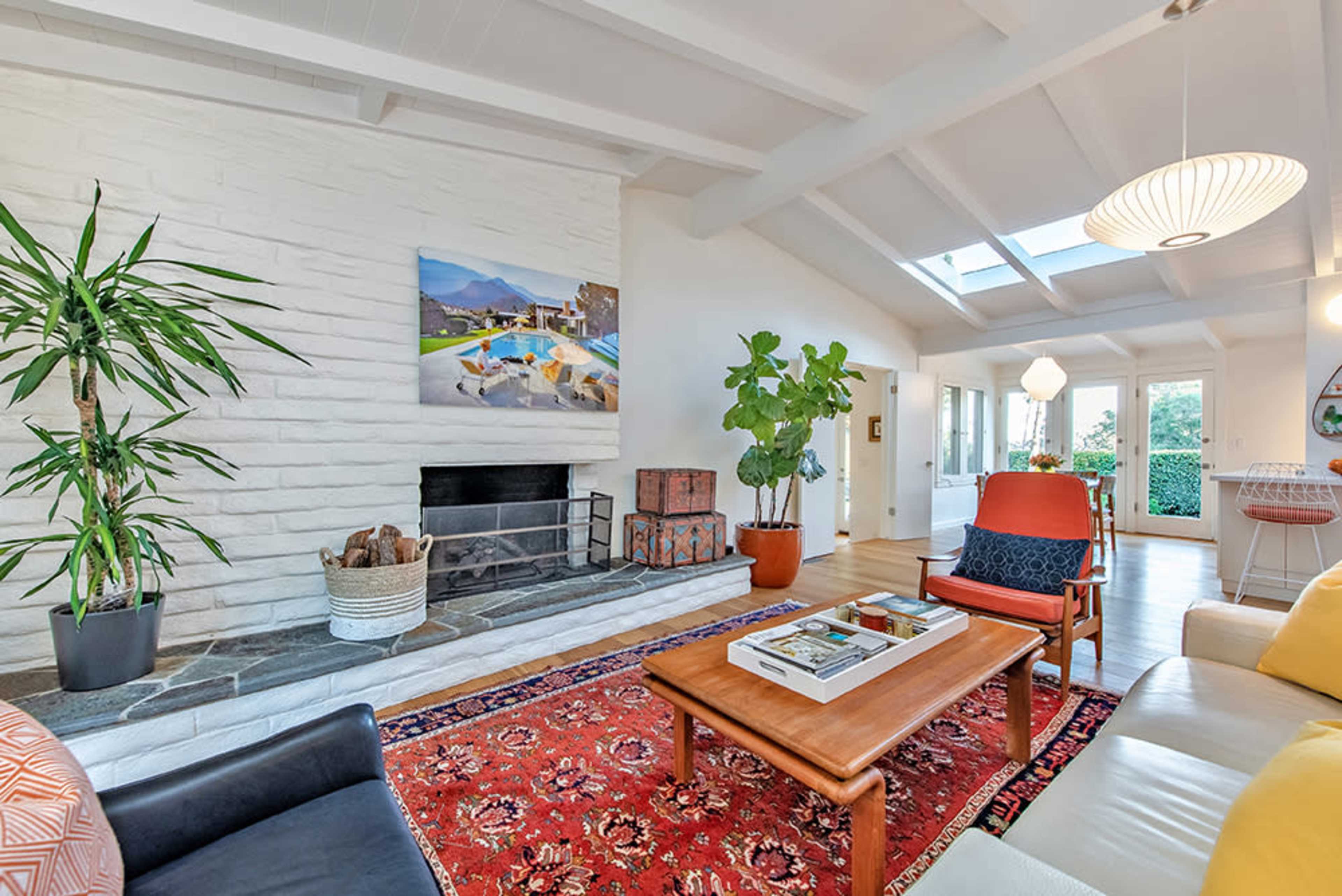 A living room features a stone fireplace, a colorful area rug, and large windows letting in natural light.