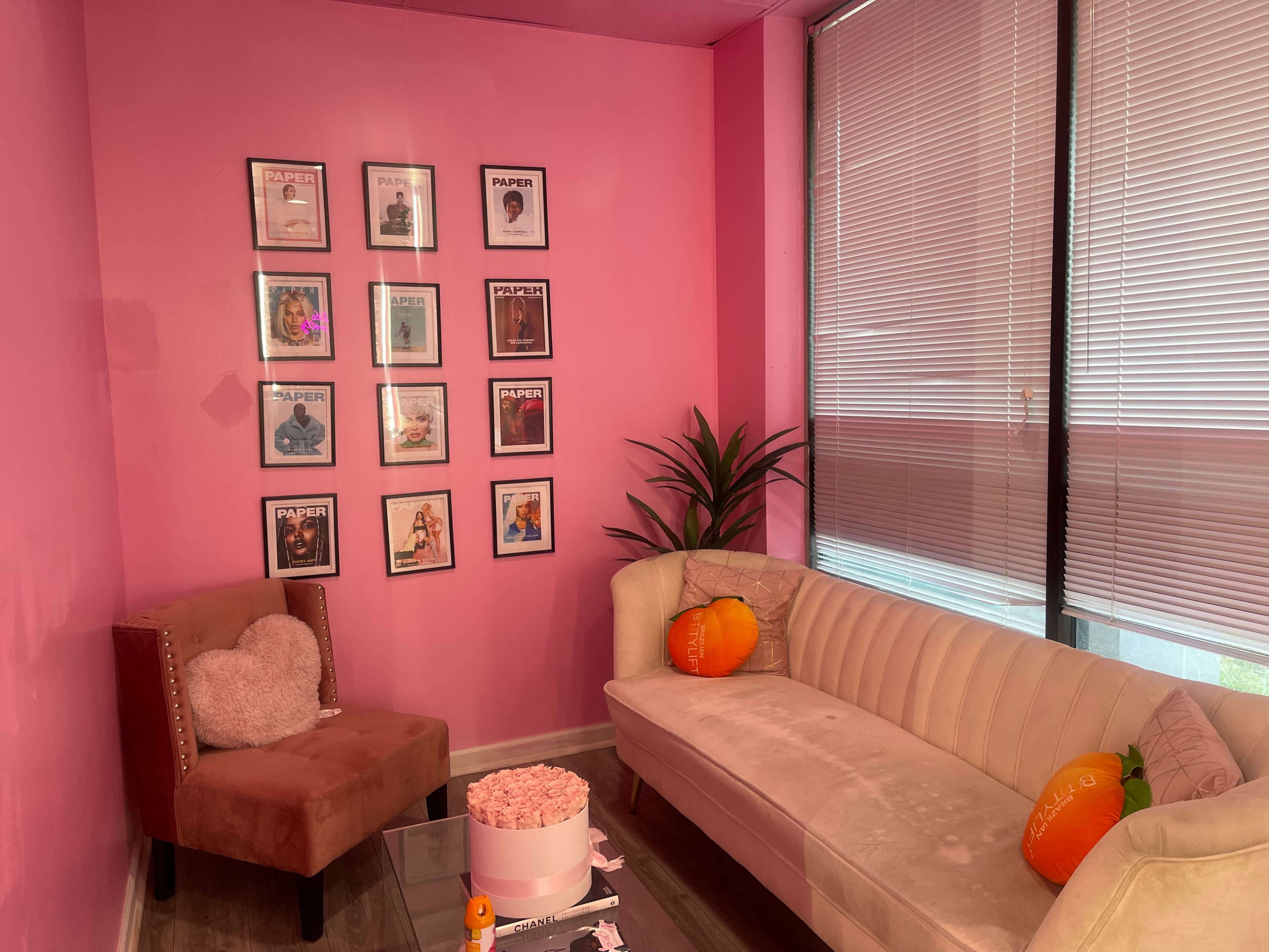 A pink-walled room with a white sofa, a decorative chair, and a wall adorned with framed pictures, along with a small glass table in the center.