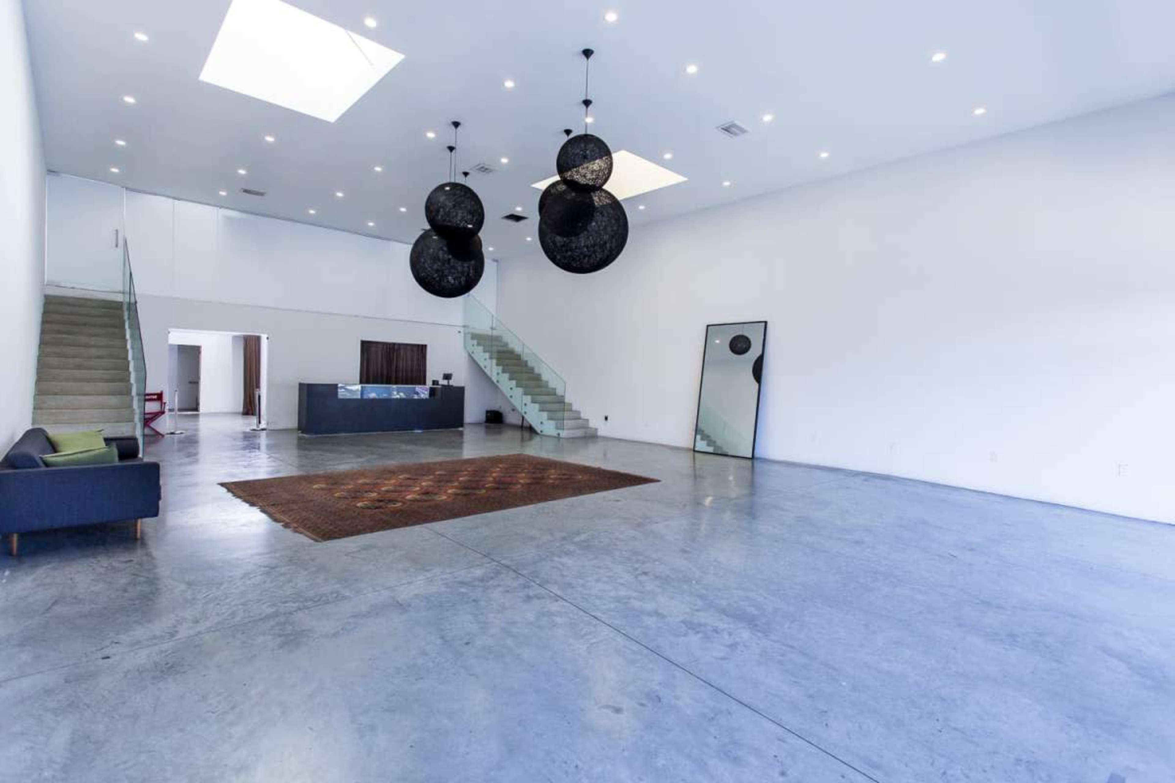 The image shows a spacious, modern interior with polished concrete floors, large windows, and three spherical hanging light fixtures.