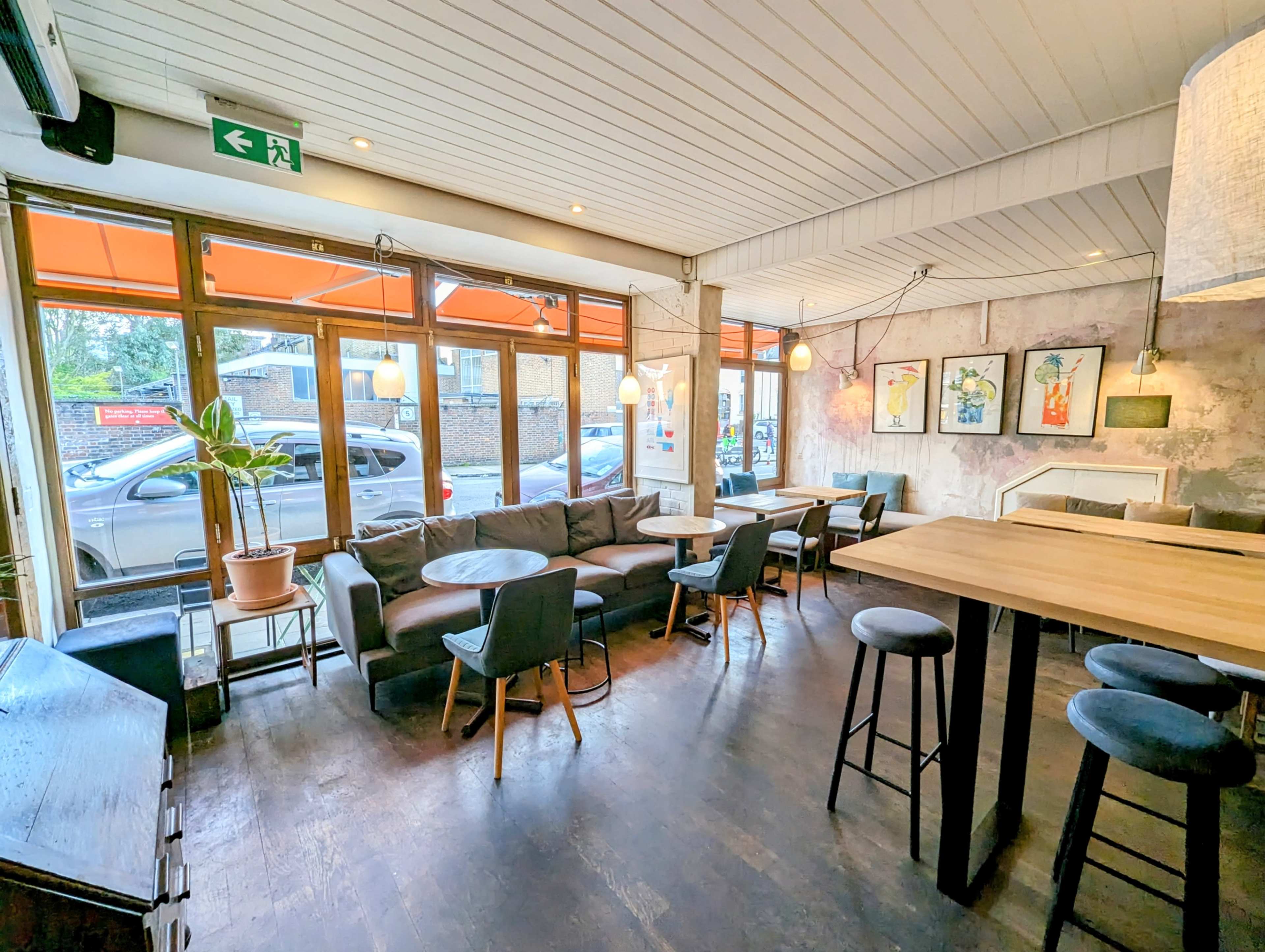 The image shows a cozy café interior with seating areas, large windows, and a view of parked cars outside.