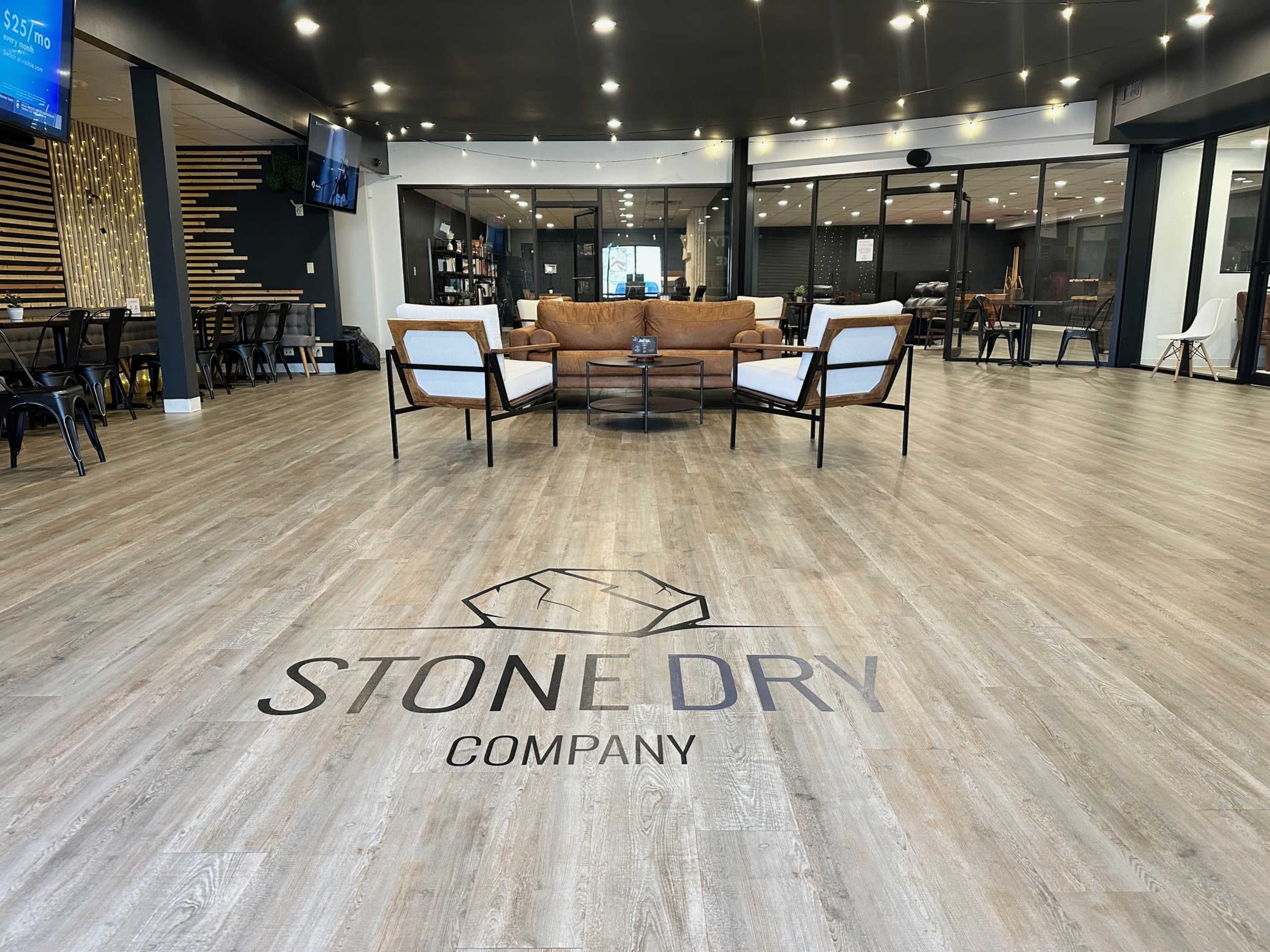 A spacious interior featuring a central seating area with a sofa and chairs, a large logo on the floor, and a modern design aesthetic.