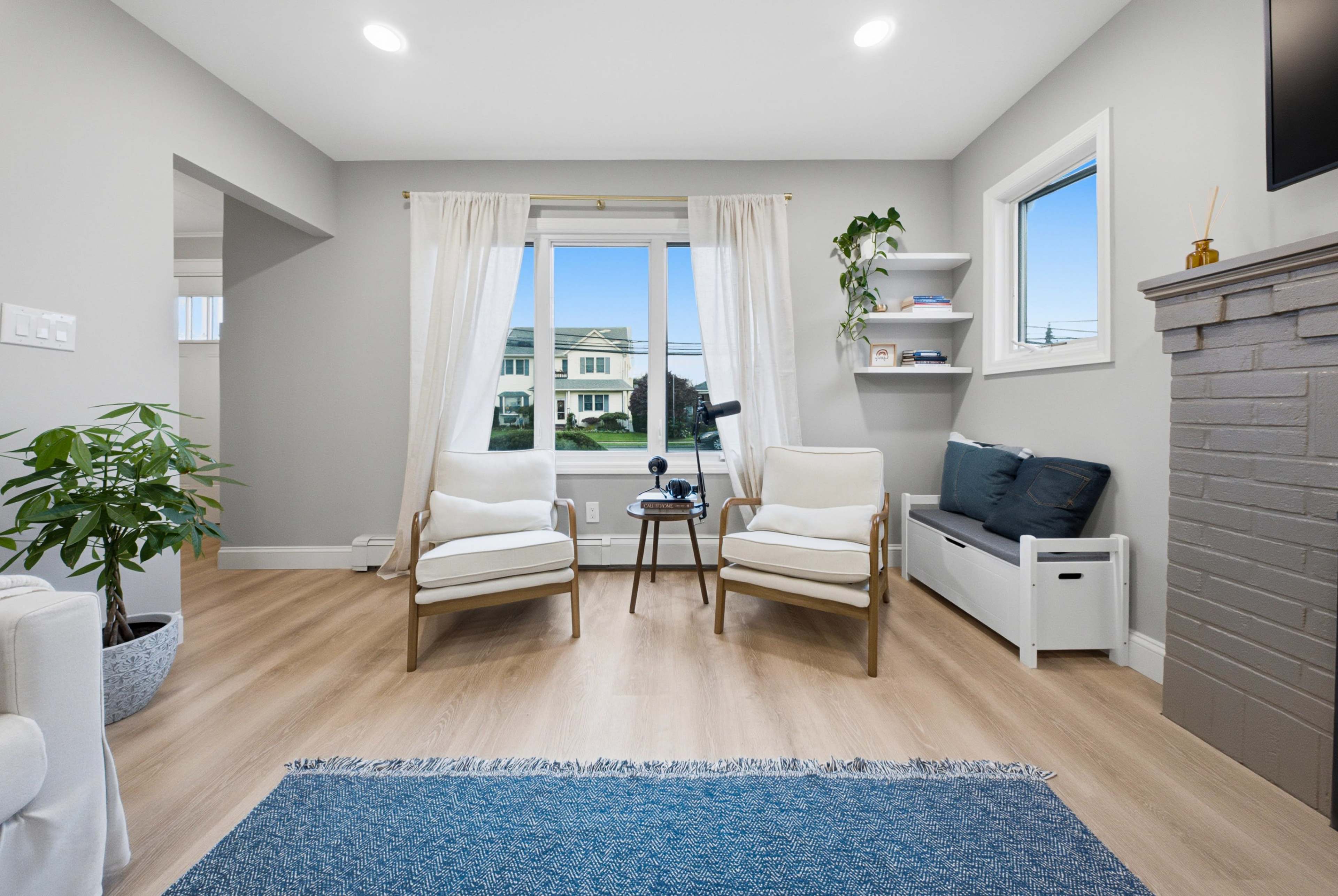 The image shows a modern living room featuring two armchairs, a small table, a window with natural light, and a plant near the corner.