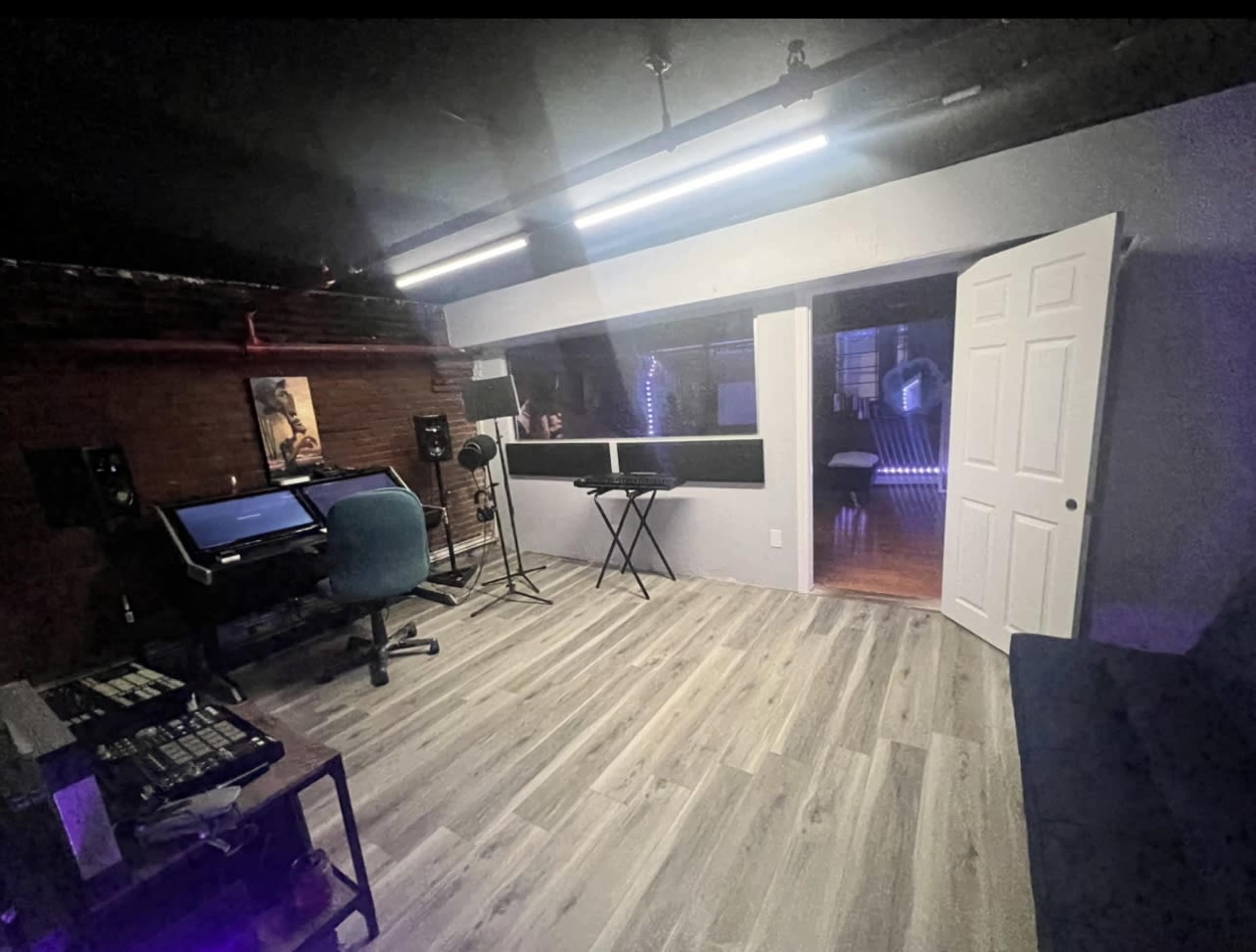 A studio room with wooden floors, a desk with a computer and audio equipment, and a door leading to another room.