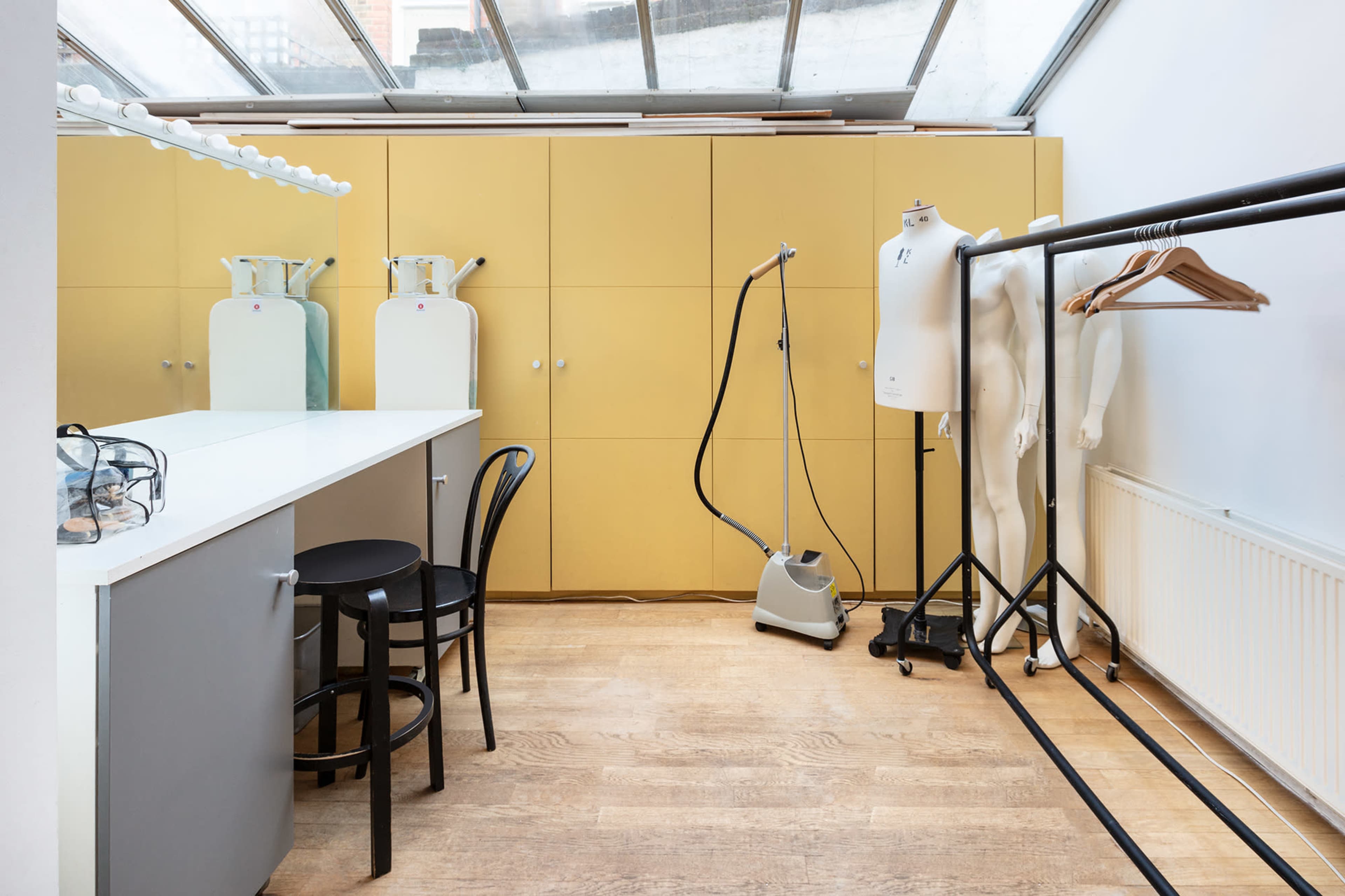 A bright room with yellow cabinetry, a white table, a steaming device, a clothing rack with hangers, and a mannequin.