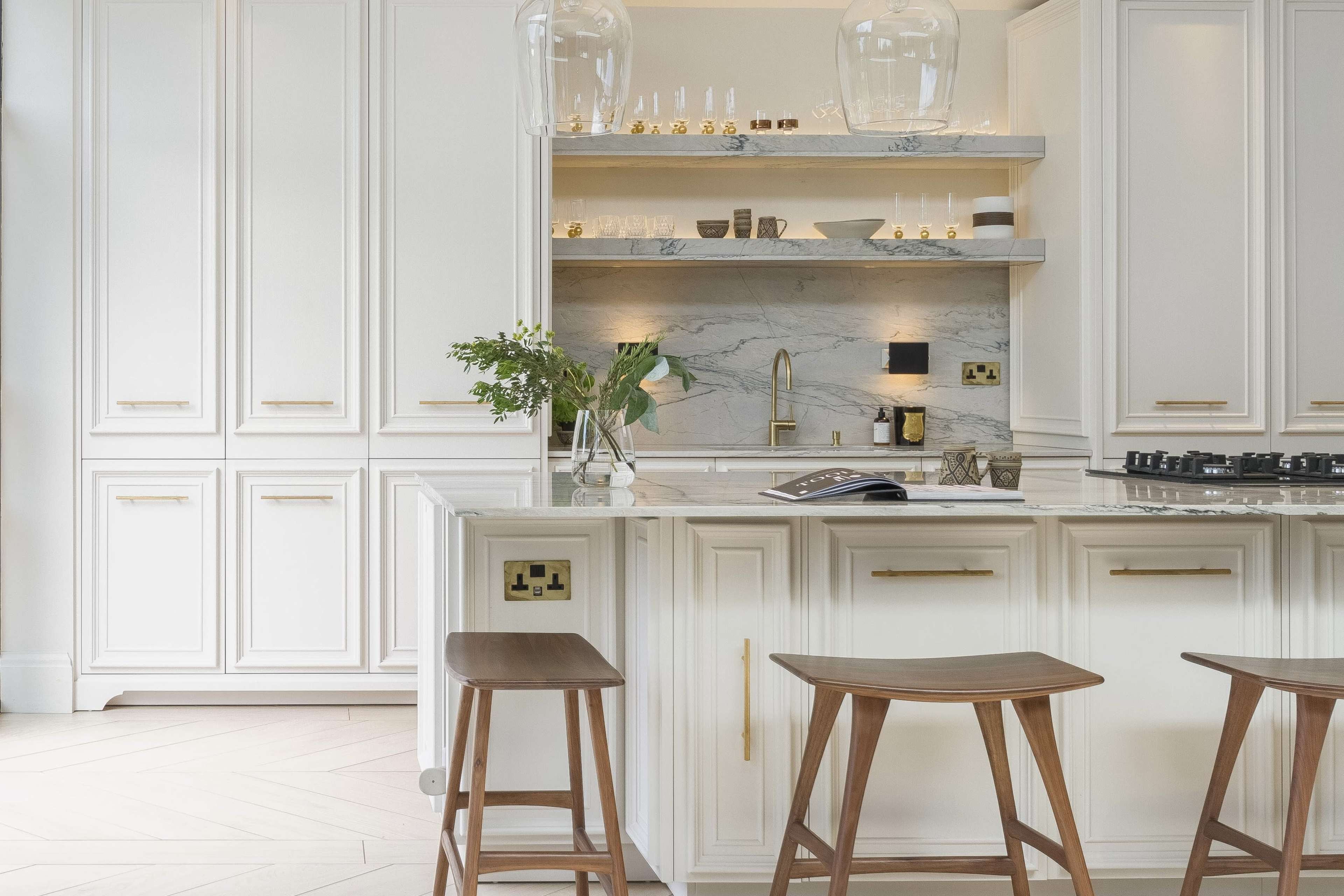 A modern kitchen features white cabinetry, a marble backsplash, and wooden bar stools around a central island.