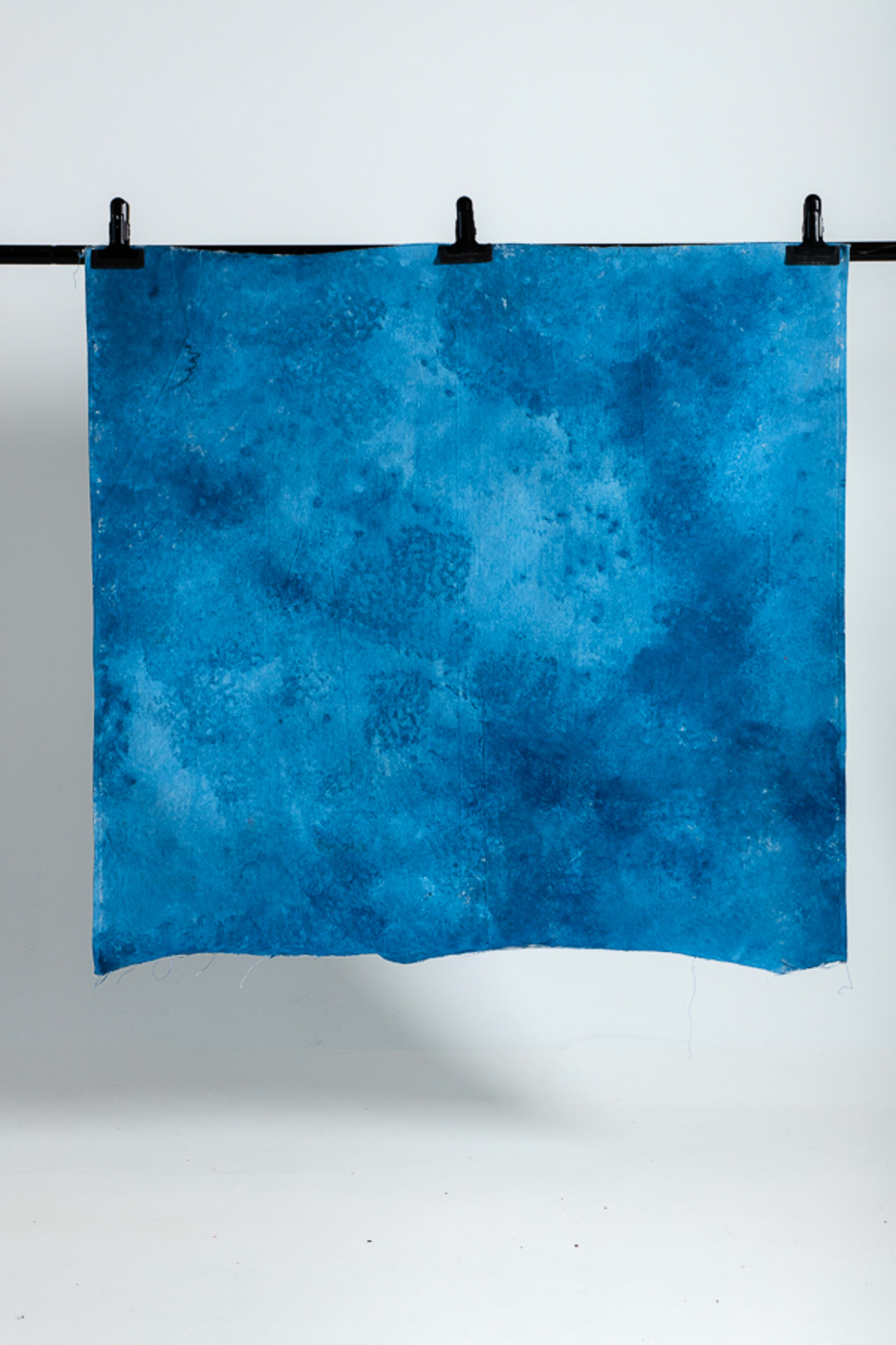 A textured blue fabric hangs on a black rod, with a solid white background.