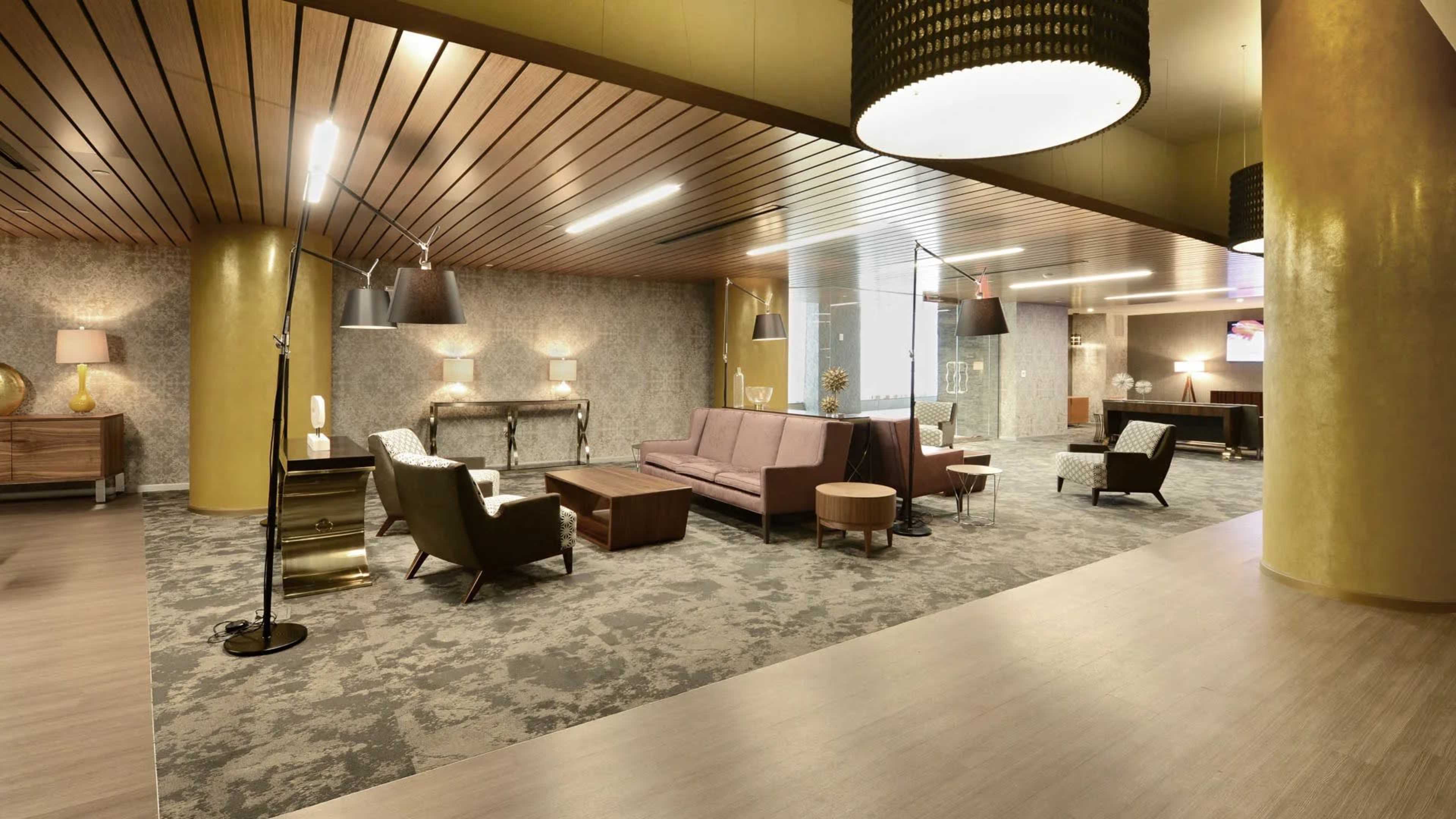 A modern lobby with various seating arrangements, decorative lamps, and a combination of polished and textured surfaces.