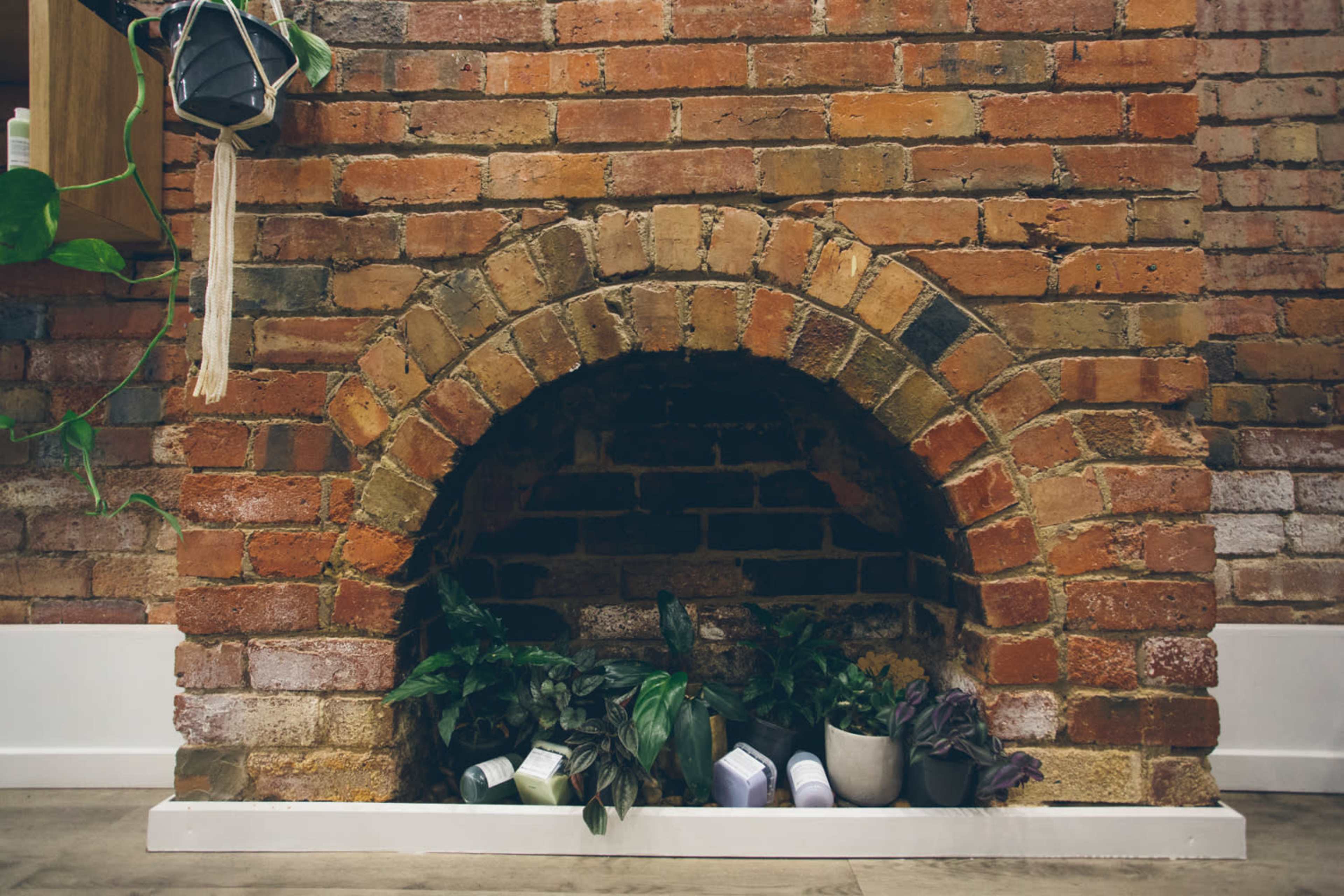 A brick fireplace with a curved arch, containing several potted plants at its base.