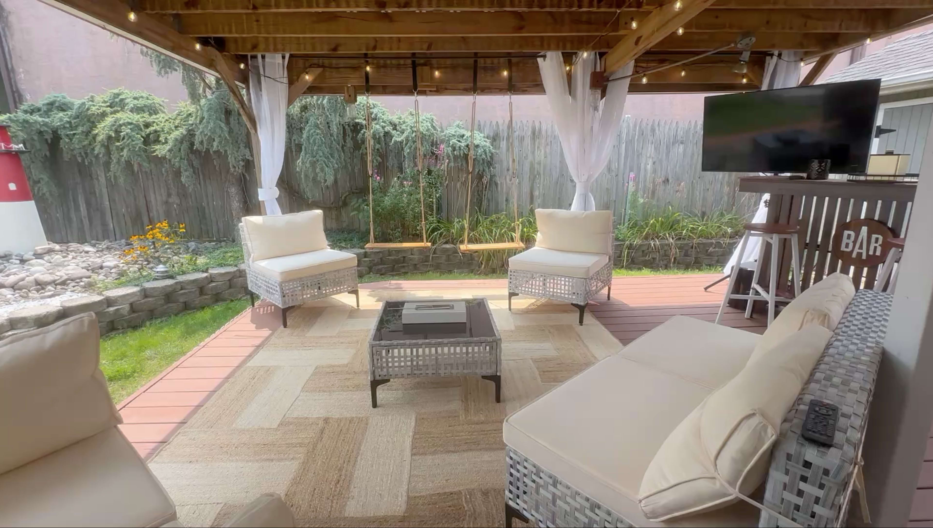 The outdoor patio features wicker furniture arranged around a coffee table, with a swing hanging from the wooden structure above.