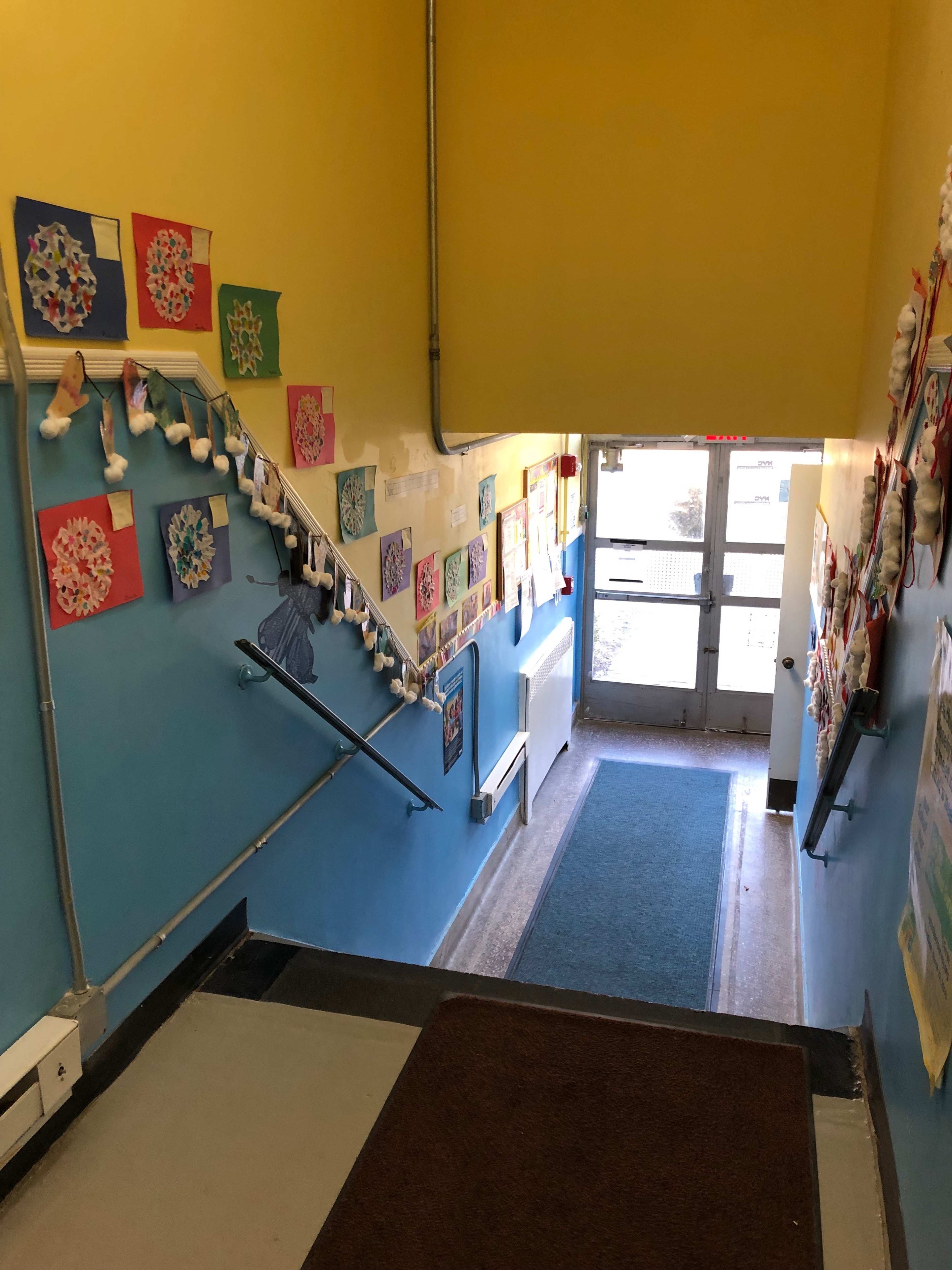 The image shows a brightly painted staircase leading down to a door, with colorful artwork hanging on the walls and a rug at the bottom of the stairs.