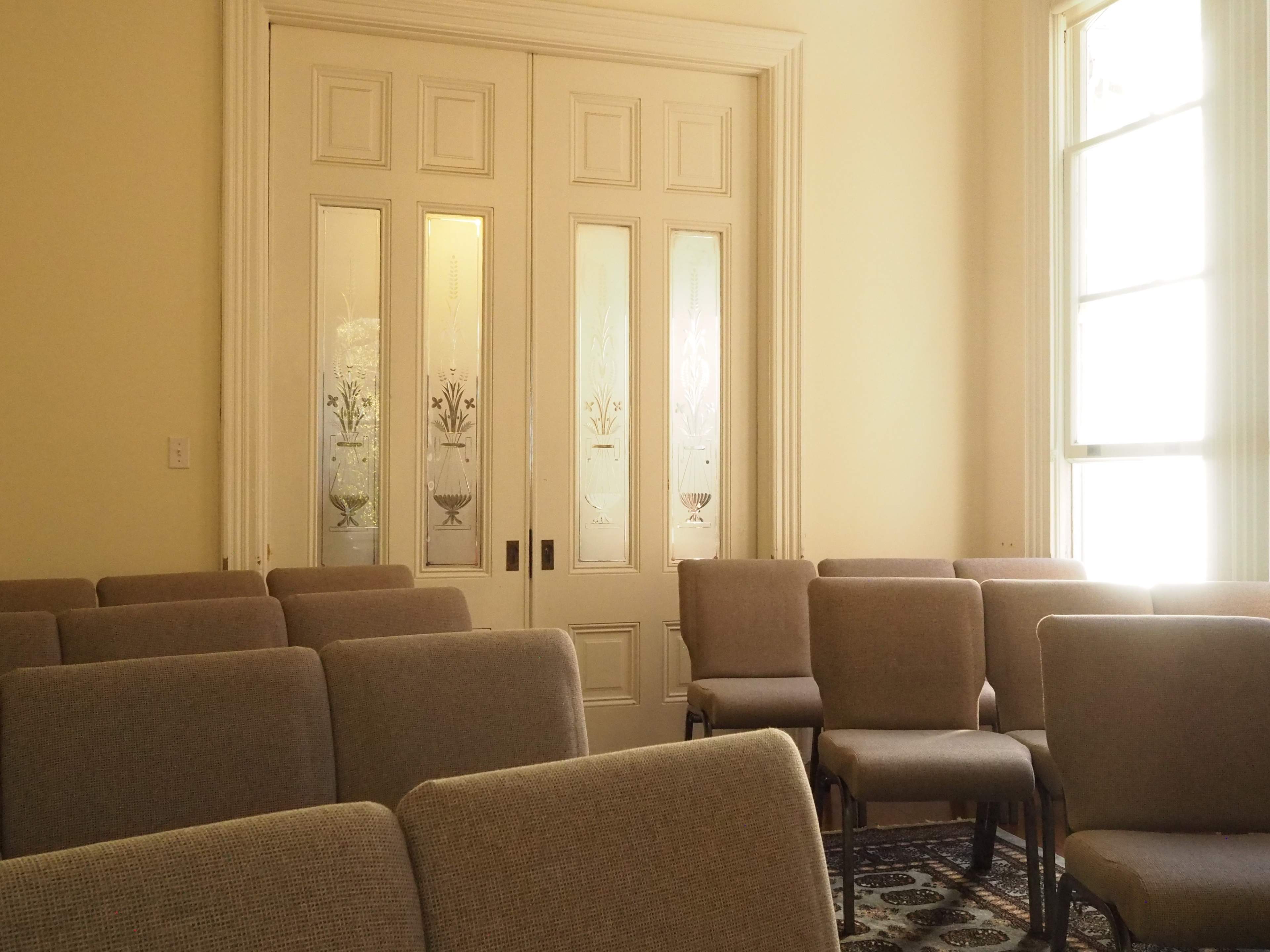 A row of cushioned chairs facing a set of elegant double doors with glass panels, located in a well-lit room.