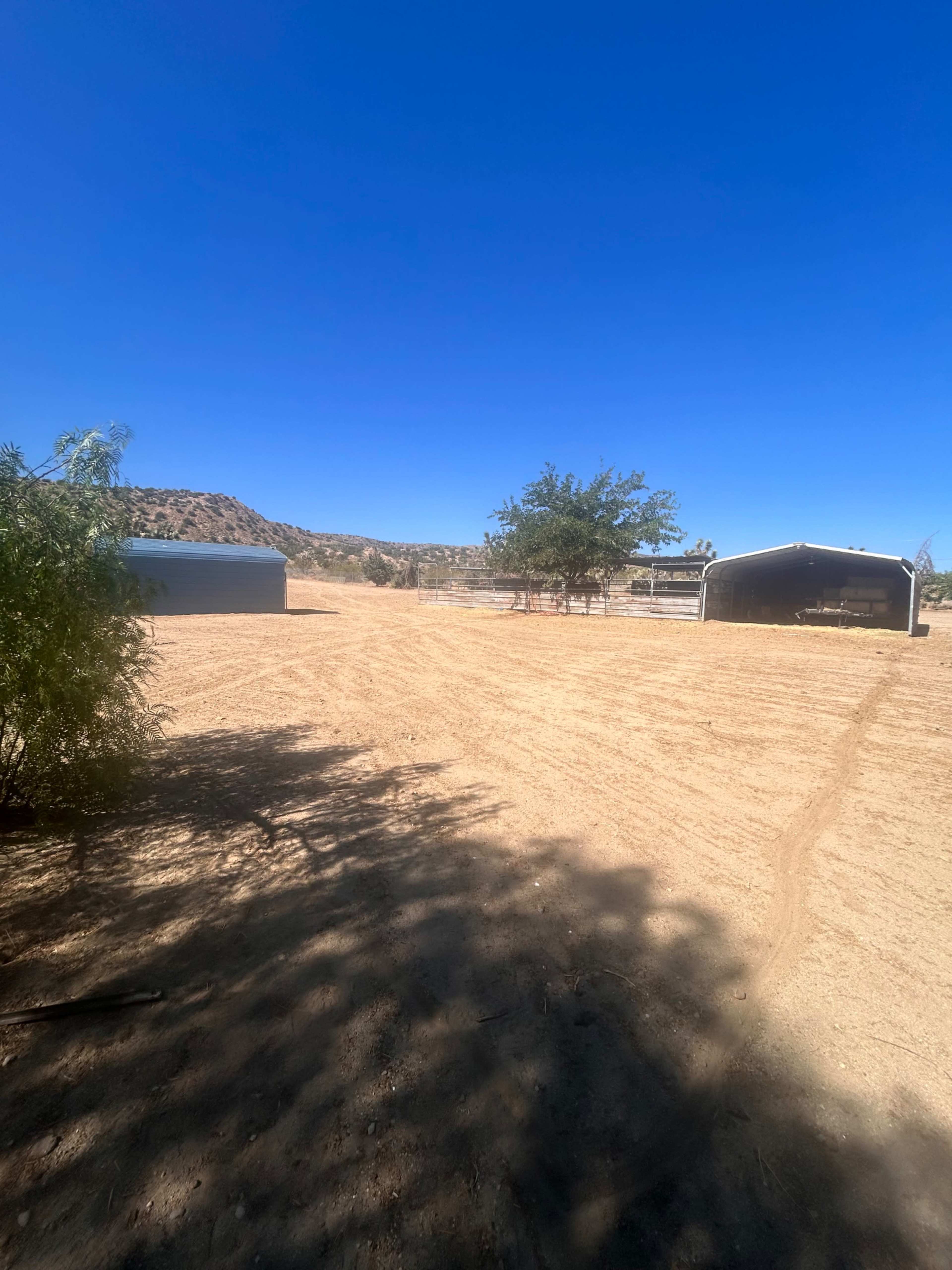 The image shows a sunlit, bare landscape with two metal structures and sparse vegetation against a clear blue sky.