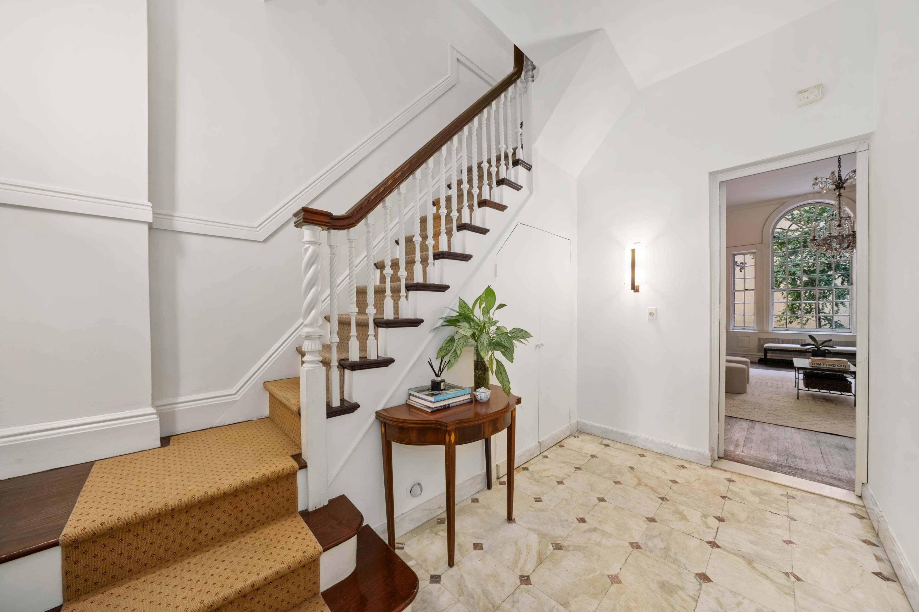 A well-lit foyer with a staircase leading to an upper level, accompanied by a small table and a plant.