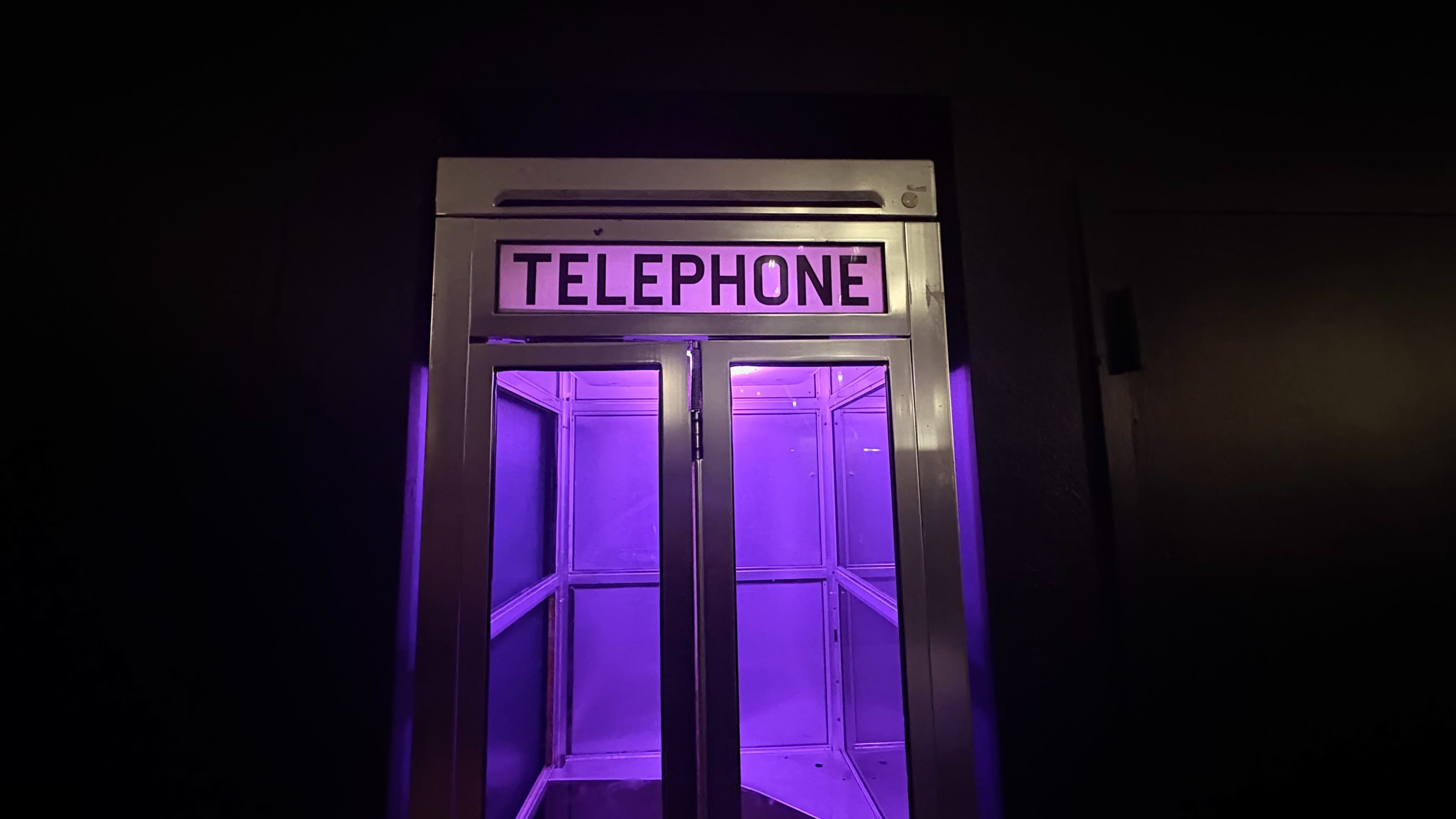 A lit telephone booth with a purple interior stands against a dark background.