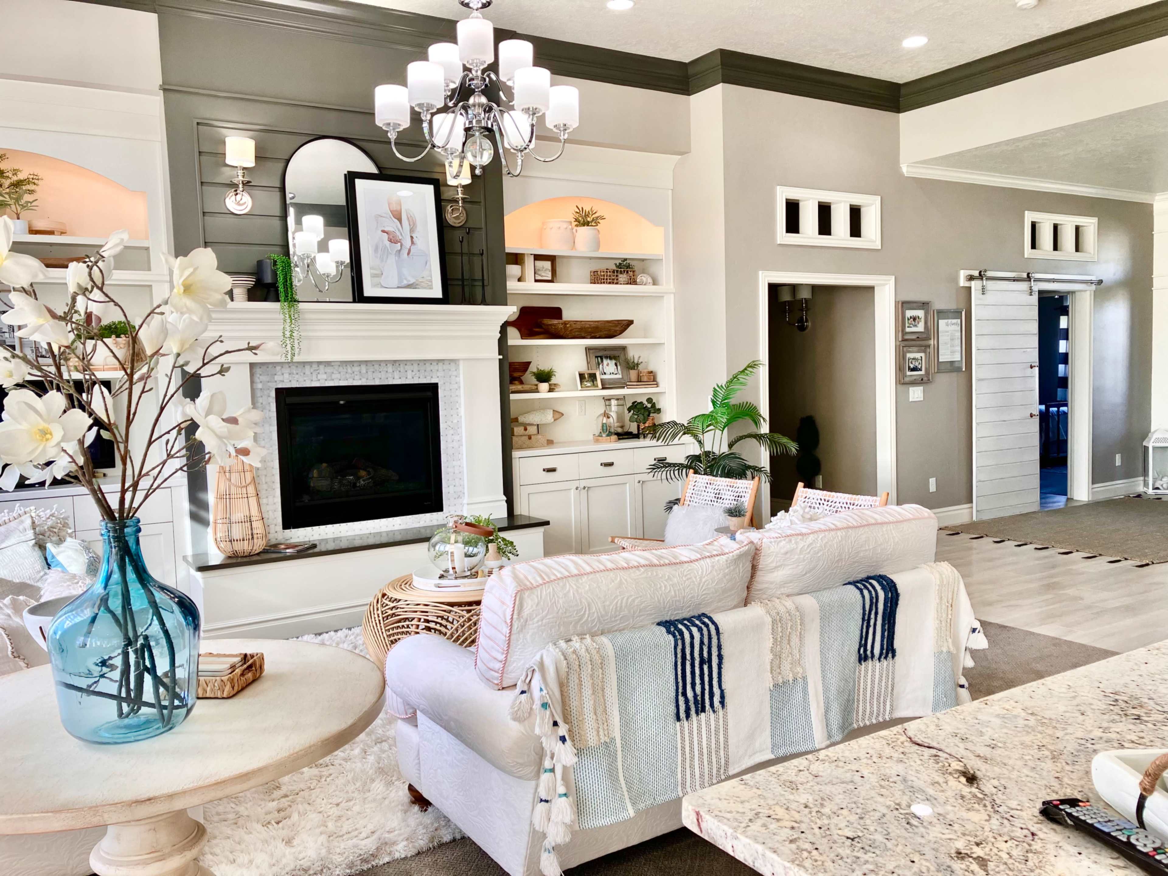 A cozy living room featuring a white sofa with decorative throw blankets, a fireplace with built-in shelves, and a light fixture hanging from the ceiling.