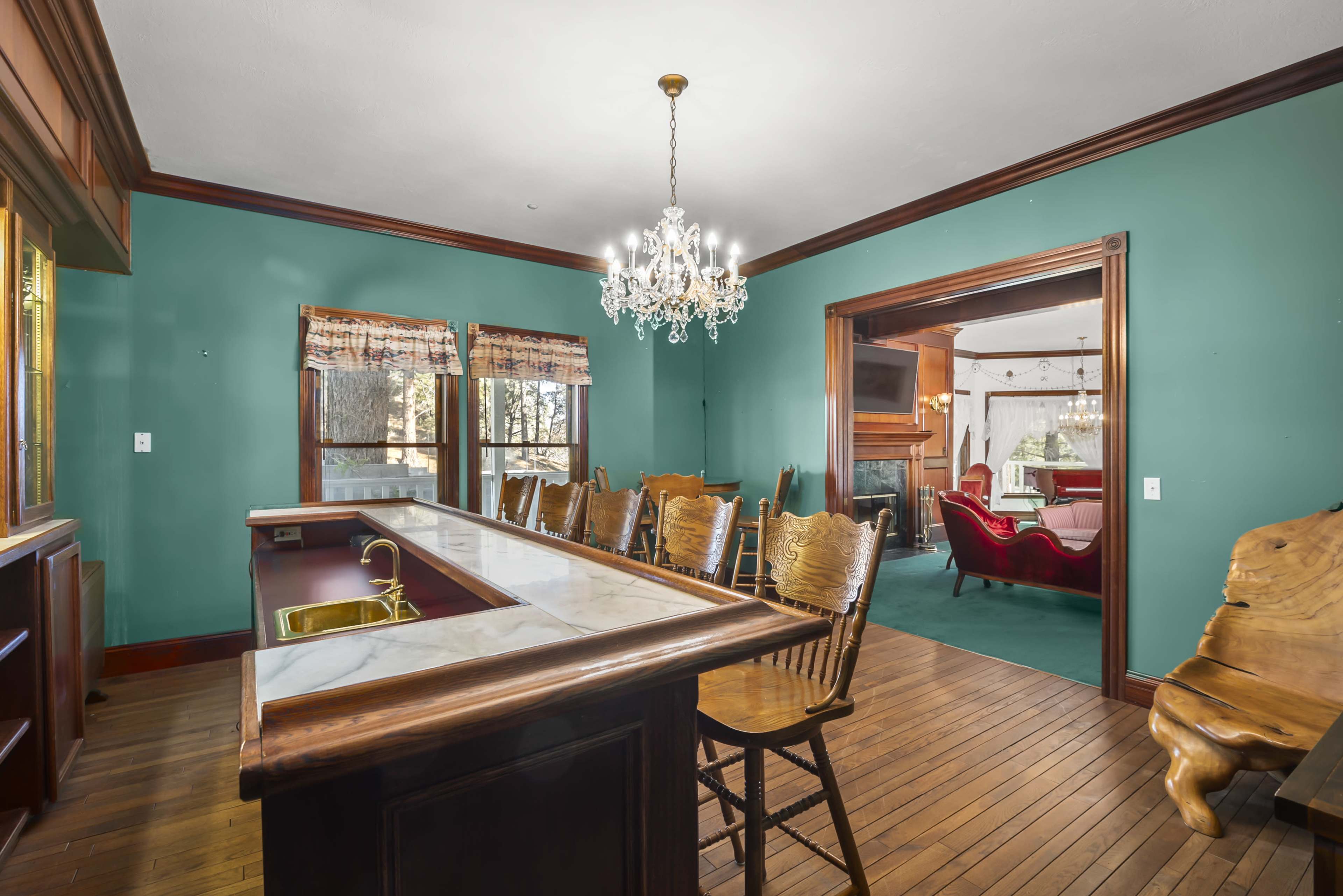 A dining area with a wooden bar and several high-backed chairs, leading into a living room with a fireplace and plush seating.