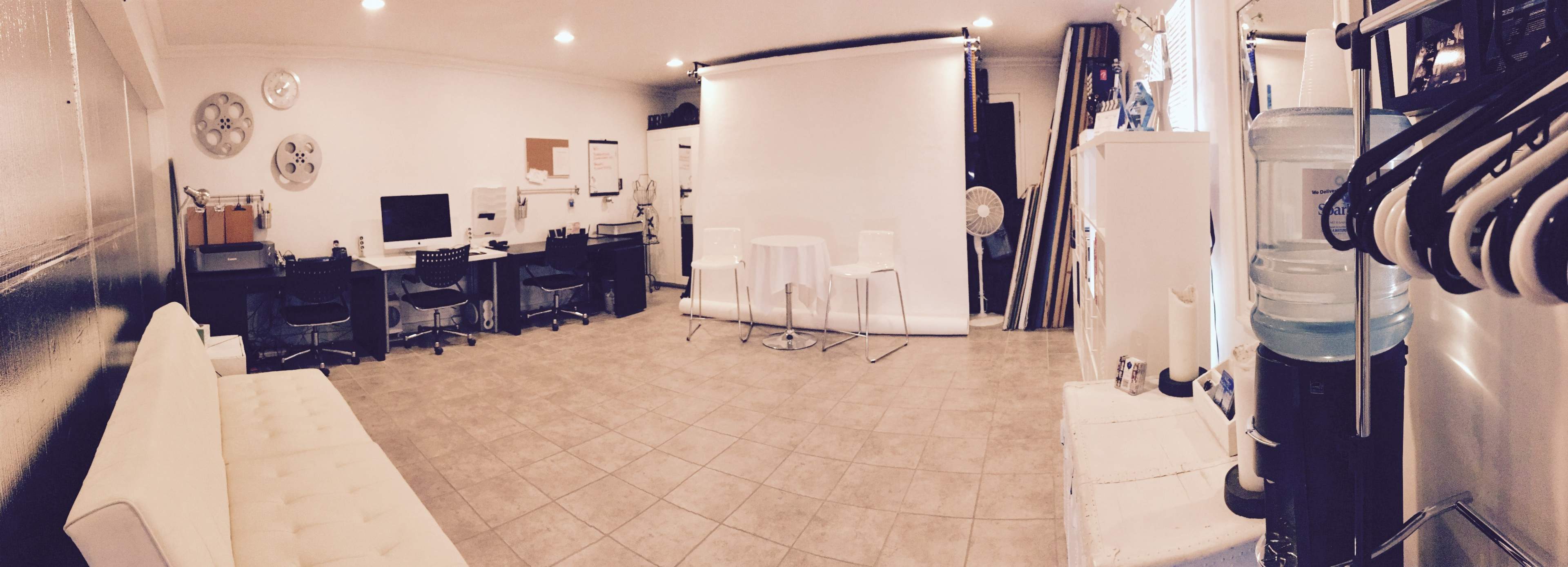 A photography studio with a white backdrop, a seating area, and workstations containing computers and other equipment.
