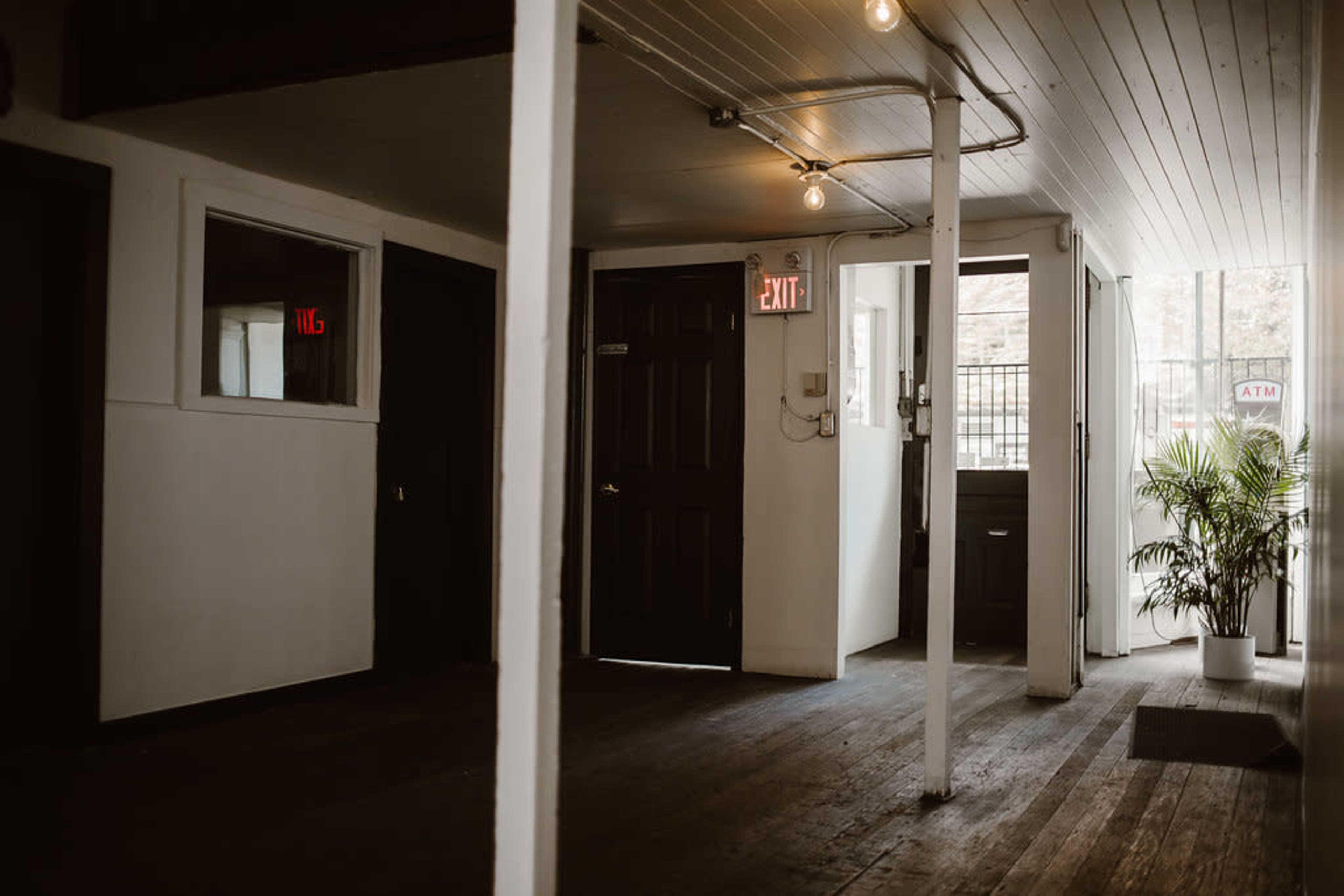 The image shows an interior space with wooden floors, a few doors, a window, and a potted plant near the entrance.