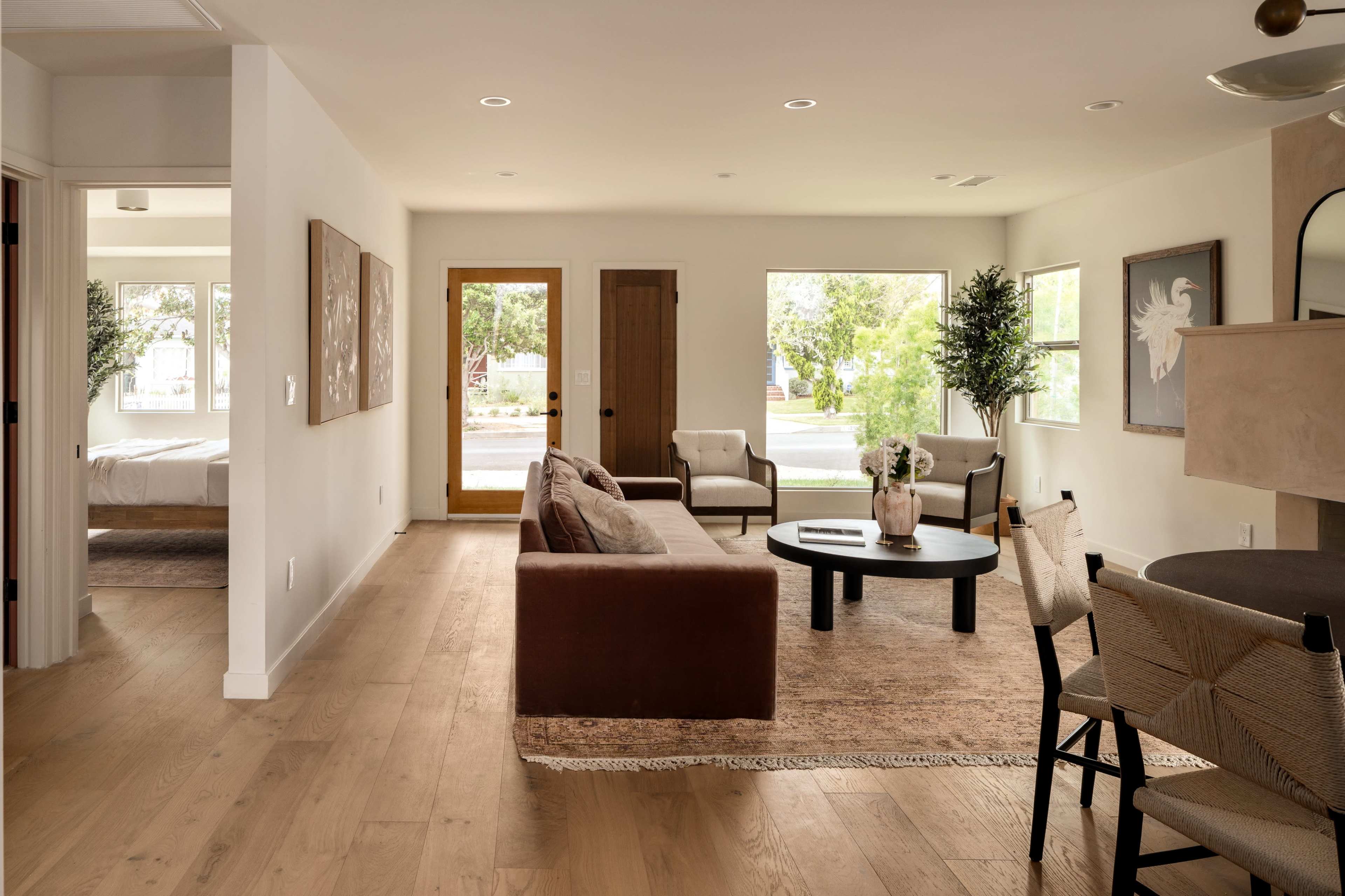 A modern, open living space with a sofa, round coffee table, and a view of an entry door, leading to another room with a bed visible in the background.