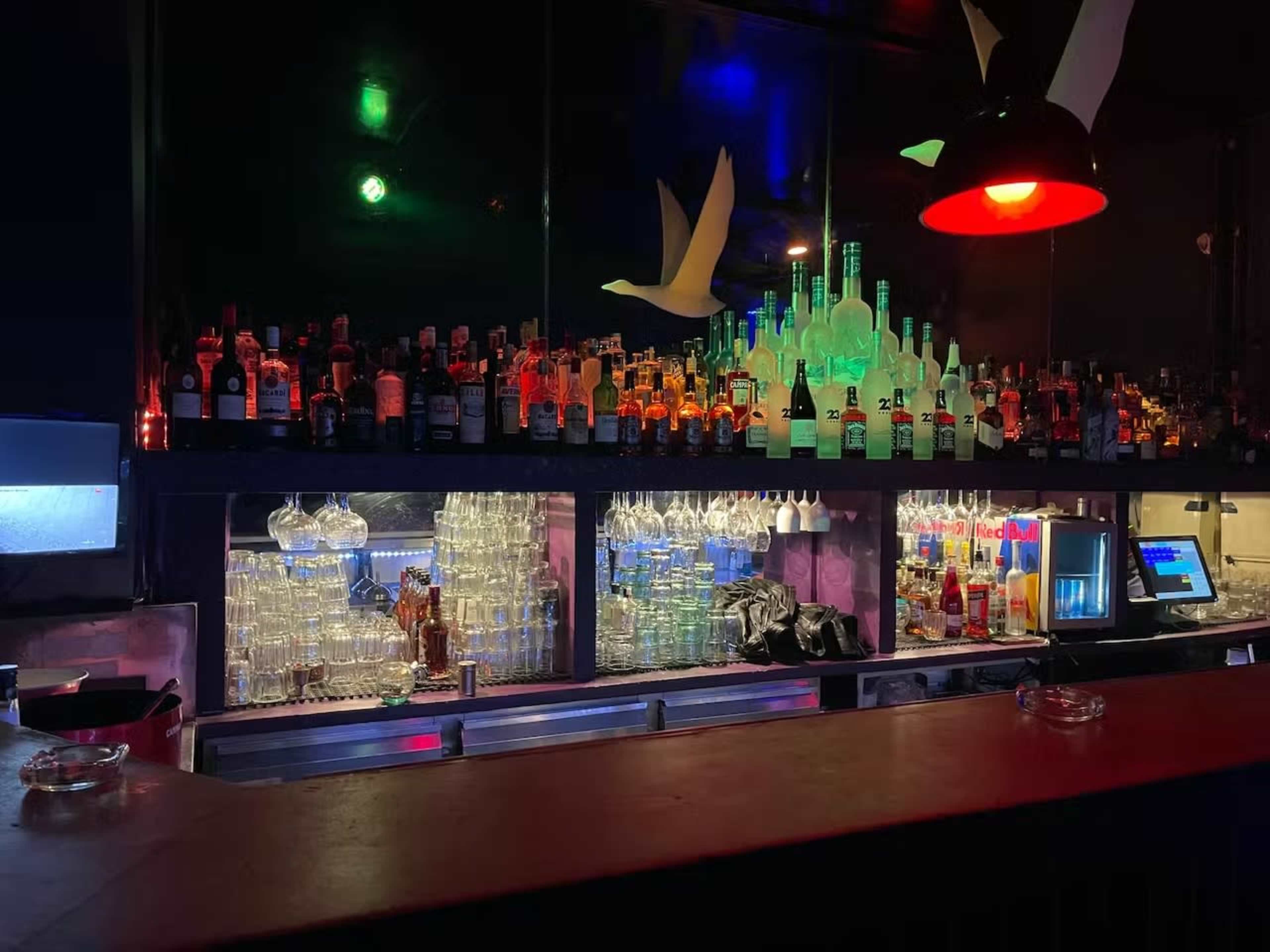 A dimly lit bar with shelves lined with various bottles of alcohol and illuminated glassware behind the counter.