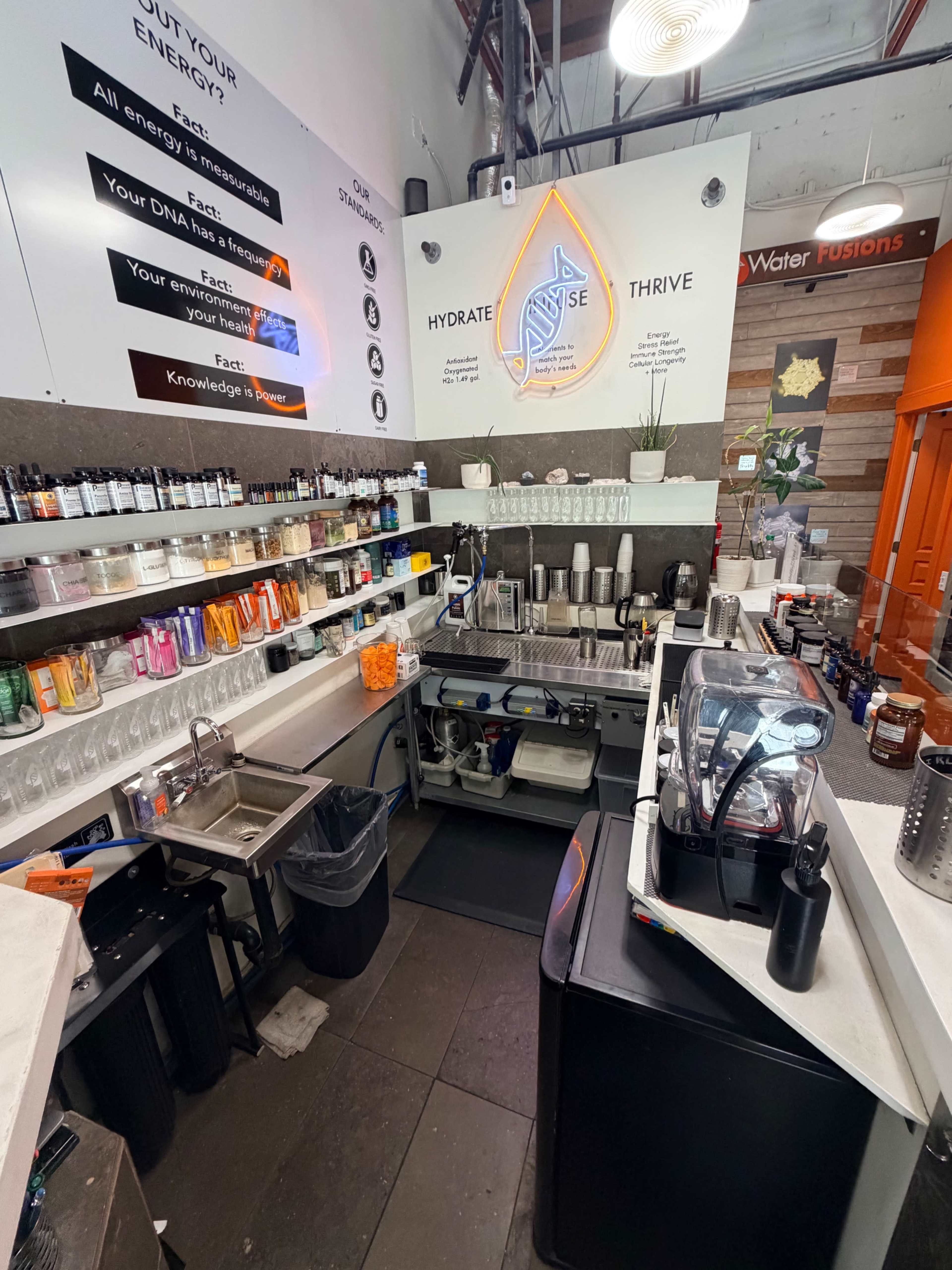 The image shows a modern beverage preparation area with shelves of ingredients, a sink, and a coffee machine.